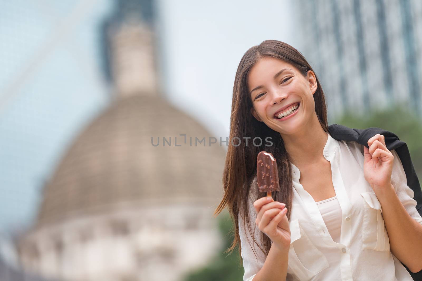 Business woman eating ice cream in Hong Kong. Young businesswoman enjoying ice-cream on at stick walking outside smiling happy in central Hong Kong. Mixed race Chinese Asian / Caucasian model on break by Maridav