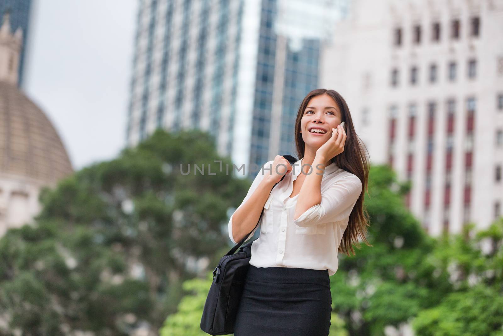 Asian business woman talking on phone walking commute to work office in Hong Kong city. Young businesswoman on smartphone happy. Multiracial Chinese Asian Caucasian female professional outside.