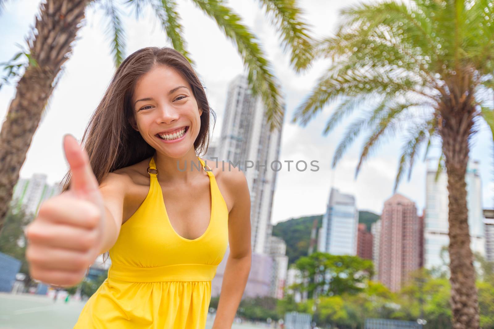 Happy chinese girl doing thumbs up in satisfaction in Hong Kong city, Asia China travel lifestyle. Young smiling multiracial woman.
