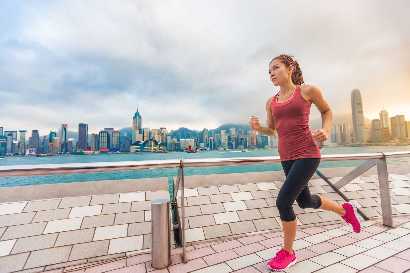 City Running - woman runner and Hong Kong skyline. Female athlete fitness athlete jogging training living healthy lifestyle on Tsim Sha Tsui Promenade and Avenue of Stars in Victoria Harbour, Kowloon.