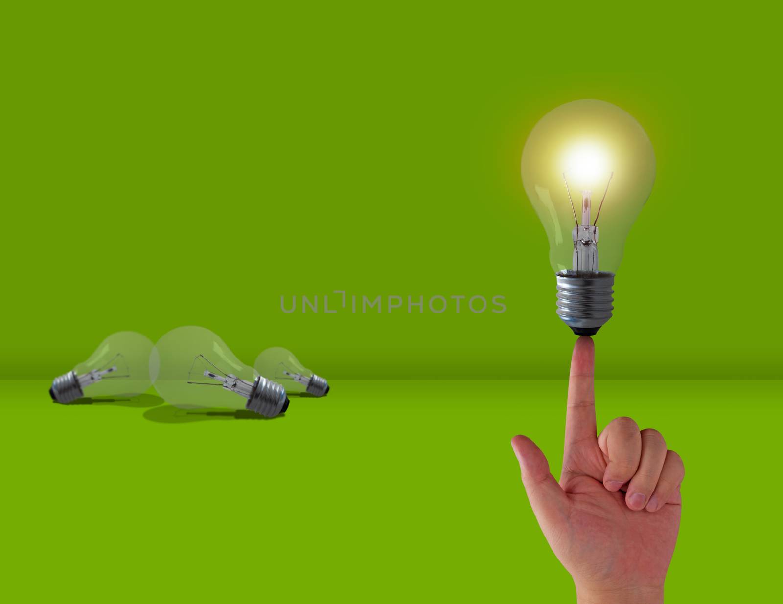 Think different concept, hand and light bulb on green background