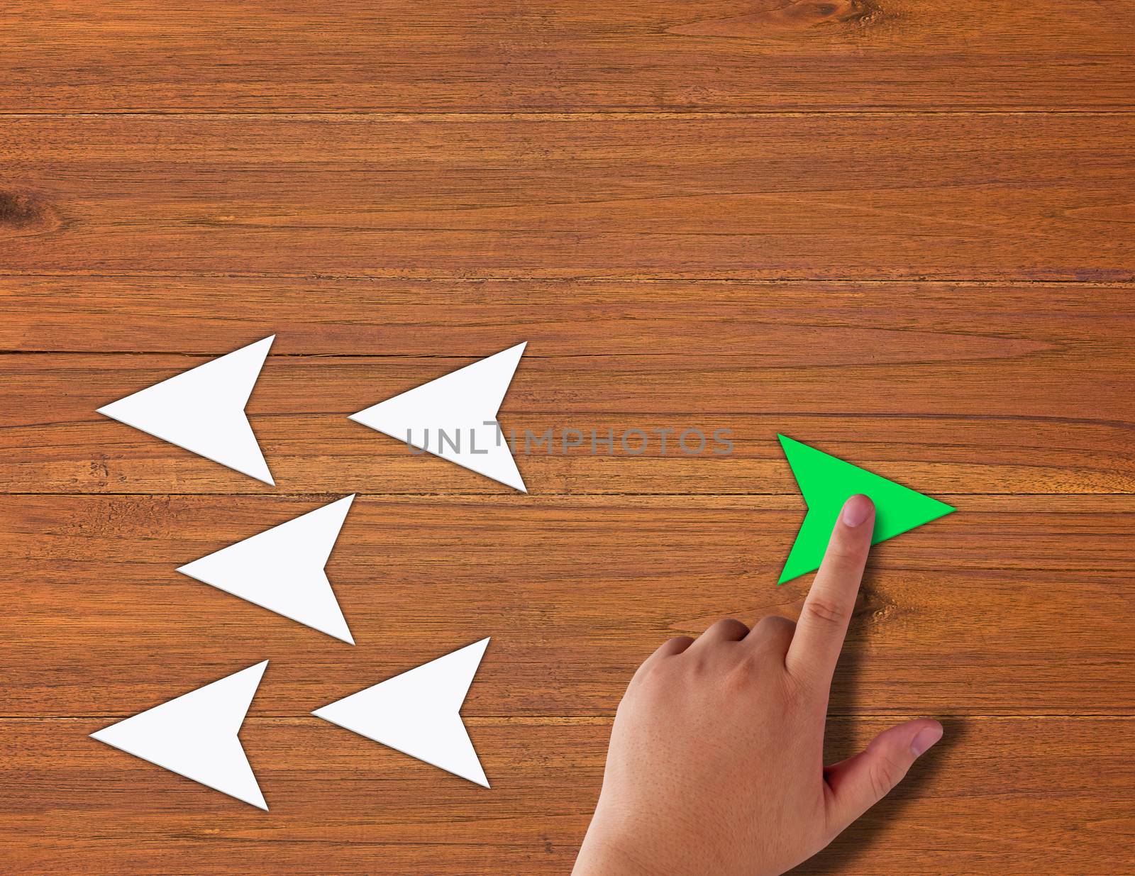 Think different concept, hand holding green paper arrow on wooden background 