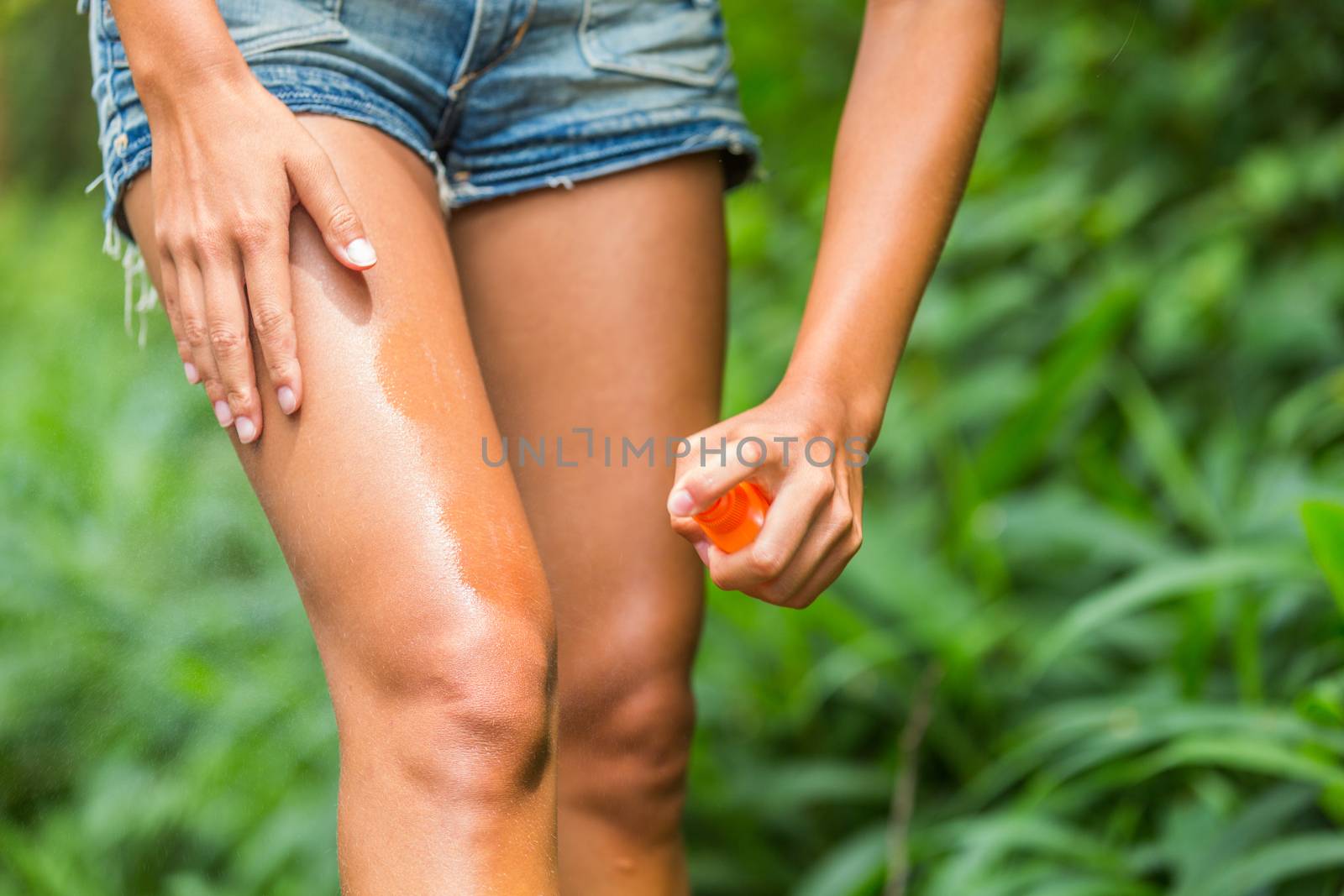 Mosquito repellent spray. Woman spraying insect repellent against zika virus bug bites virus on legs skin outdoor in nature forest using spray bottle.