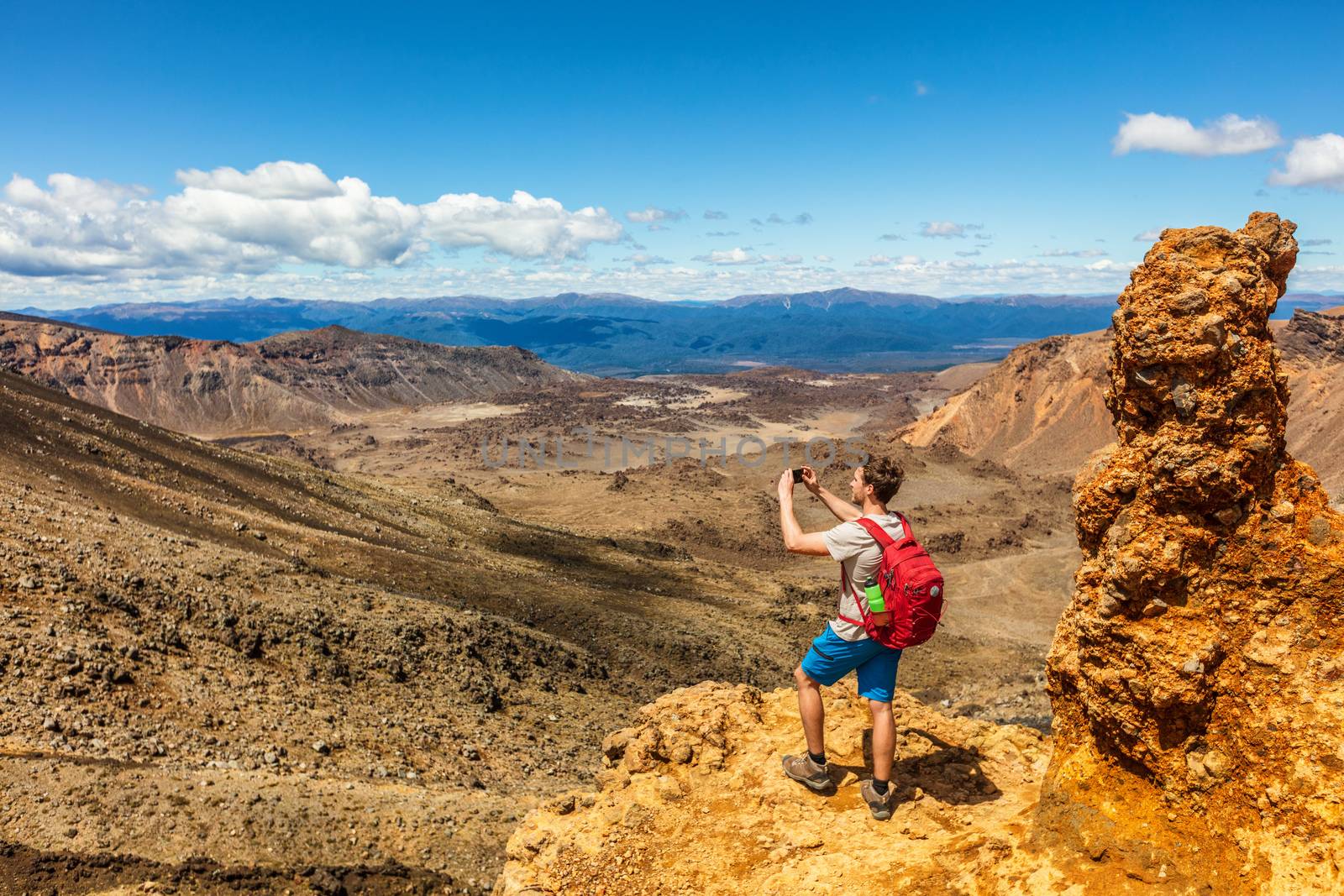 New Zealand Tongariro Alpine Crossing hike trail nature landscape hiker man taking picture of background. Happy tramper filming phone photo at volcanic mountains . Summer adventure Travel.