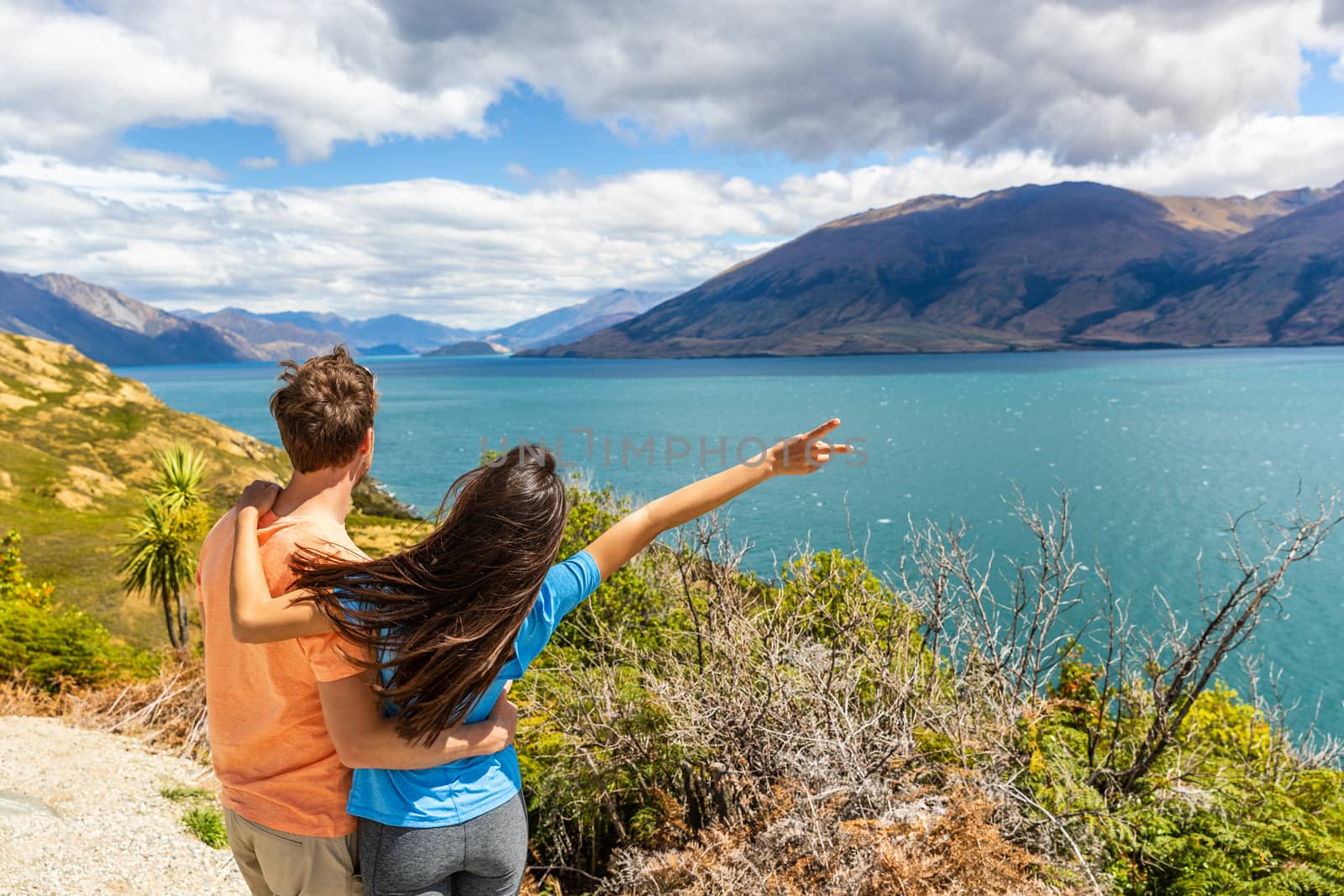 Travel couple enjoying wanderlust road trip in New Zealand, woman with arm up in excitement at Lake view in NZ. Trampers traveling summer destination landscape by Maridav