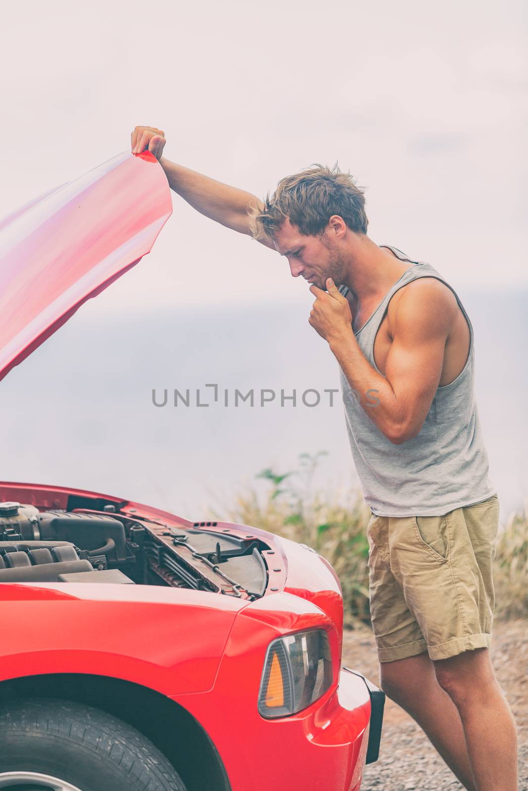 Car breakdown problem. Road trip travel young man on side of the road with broken engine looking at motor in open hood repairing issue.