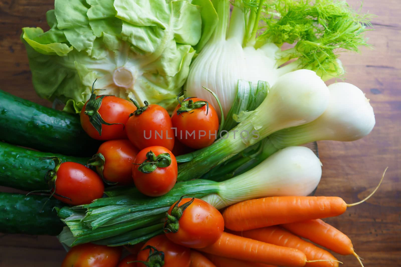 Healthy nutrition with fresh raw vegetables: flat lay top view of a group of salad ingredients, lettuce, tomatoes, cucumbers, fennel, spring onions, and carrots on a wooden table copy space