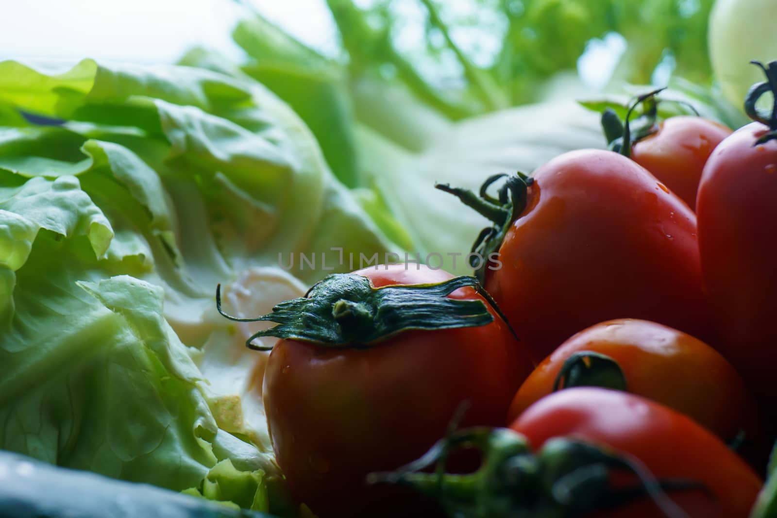 Healthy nutrition with fresh raw vegetables: close up detail of a tomato in the foreground on green vegetables in background bokeh effect by robbyfontanesi