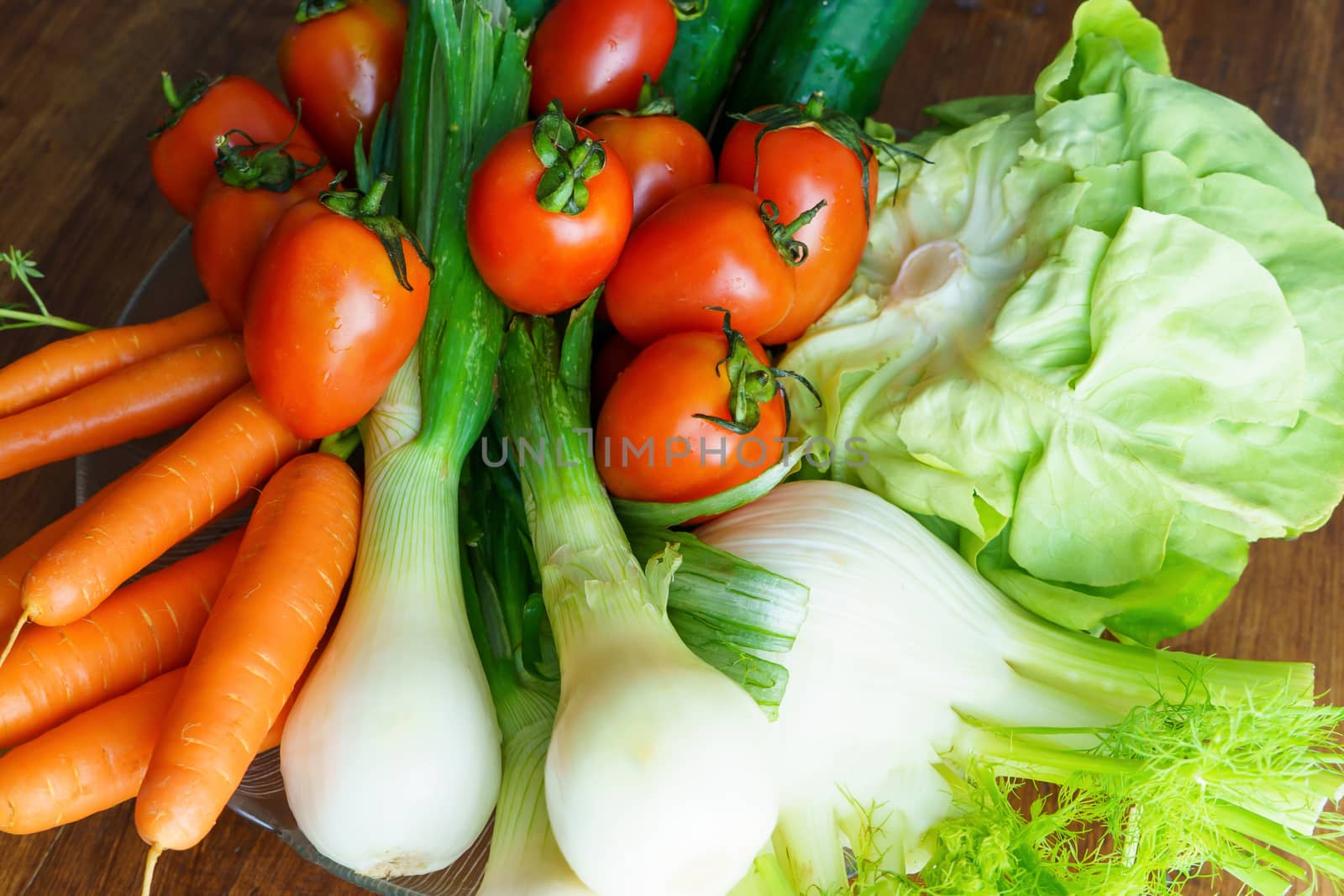 Healthy nutrition with fresh raw vegetables: a low angle close up view of a group of salad ingredients, lettuce, tomatoes, cucumbers, fennel, spring onions, and carrots by robbyfontanesi