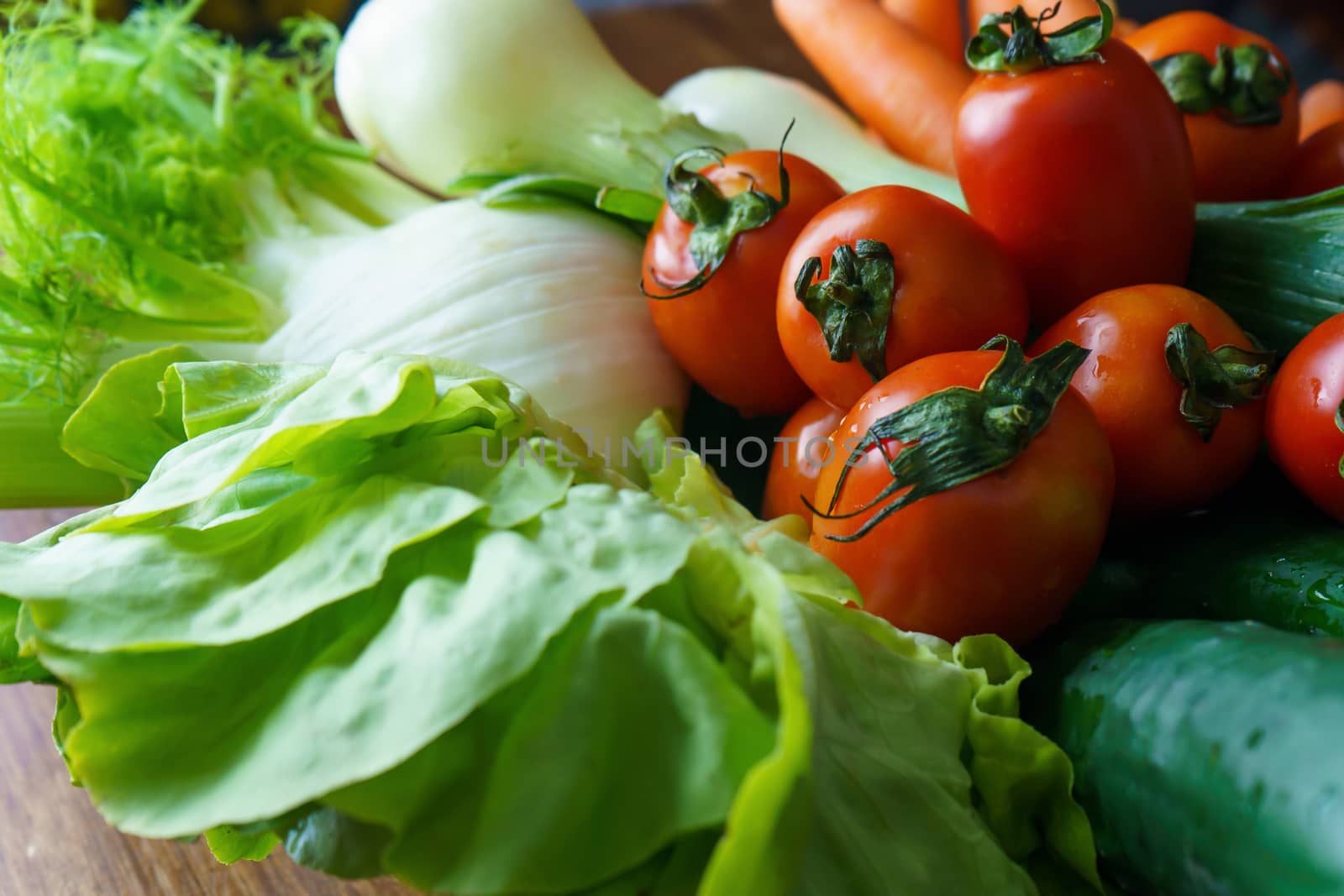 Healthy nutrition with fresh raw vegetables: a low angle close up view of a group of salad ingredients, lettuce, tomatoes, cucumbers, fennel, spring onions, and carrots by robbyfontanesi