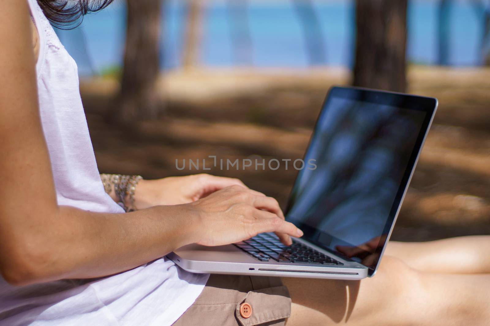 Close up of freelance woman working in vacation on the laptop sitting in a pine forest on the sea, smart working lifestyle concept theme and life choice