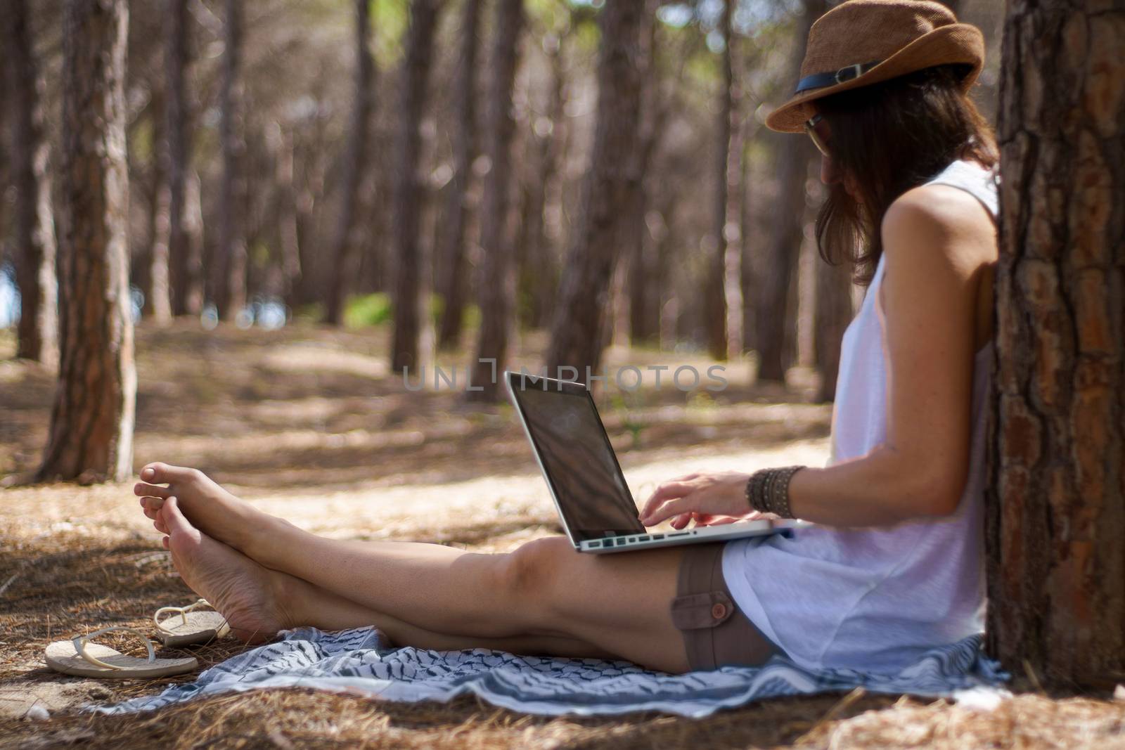 Freelance woman working in vacation on the laptop sitting in a pine forest on the sea, smart working lifestyle concept theme and life choice