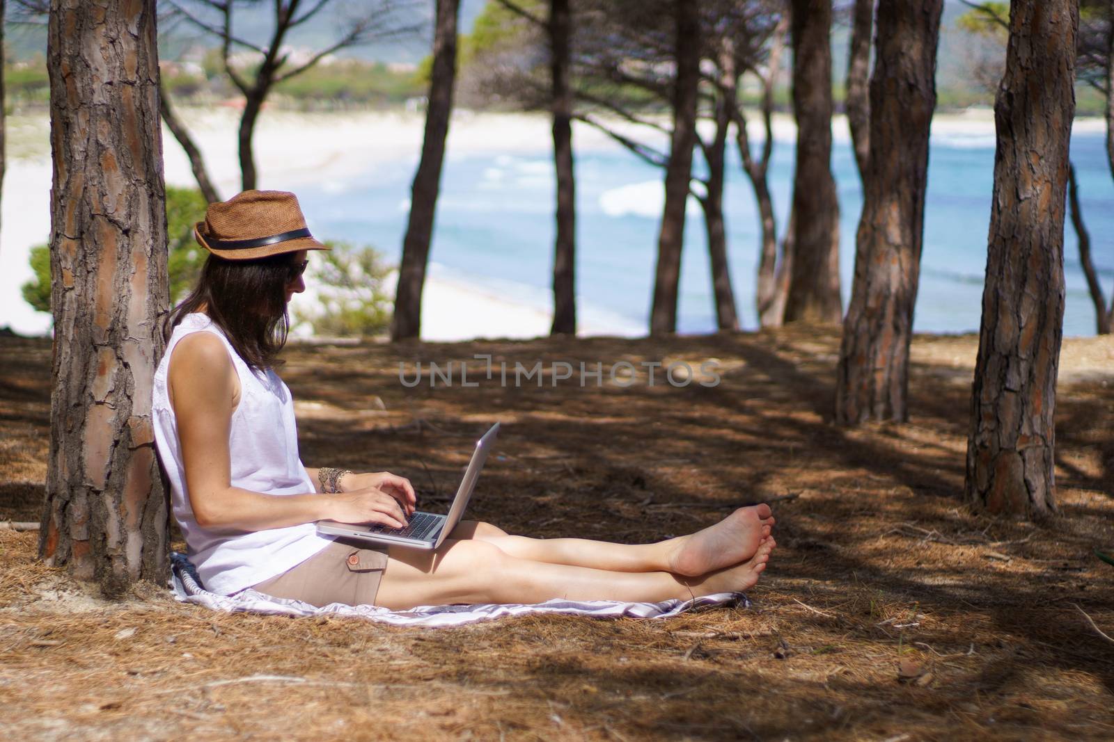 Freelance woman working in vacation on the laptop sitting in a pine forest on the sea, smart working lifestyle concept theme and life choice