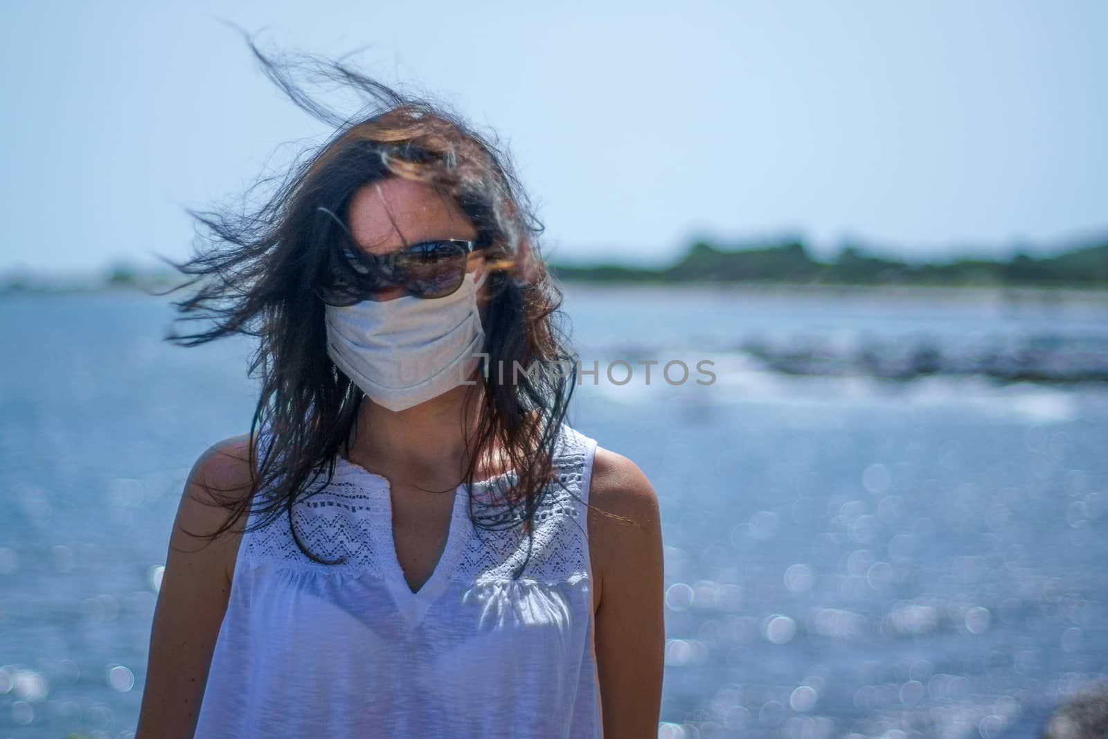 Coronavirus seaside holidays: half-length shot of a woman at the beach with the mask for Covid-19 pandemic with cloudy sky