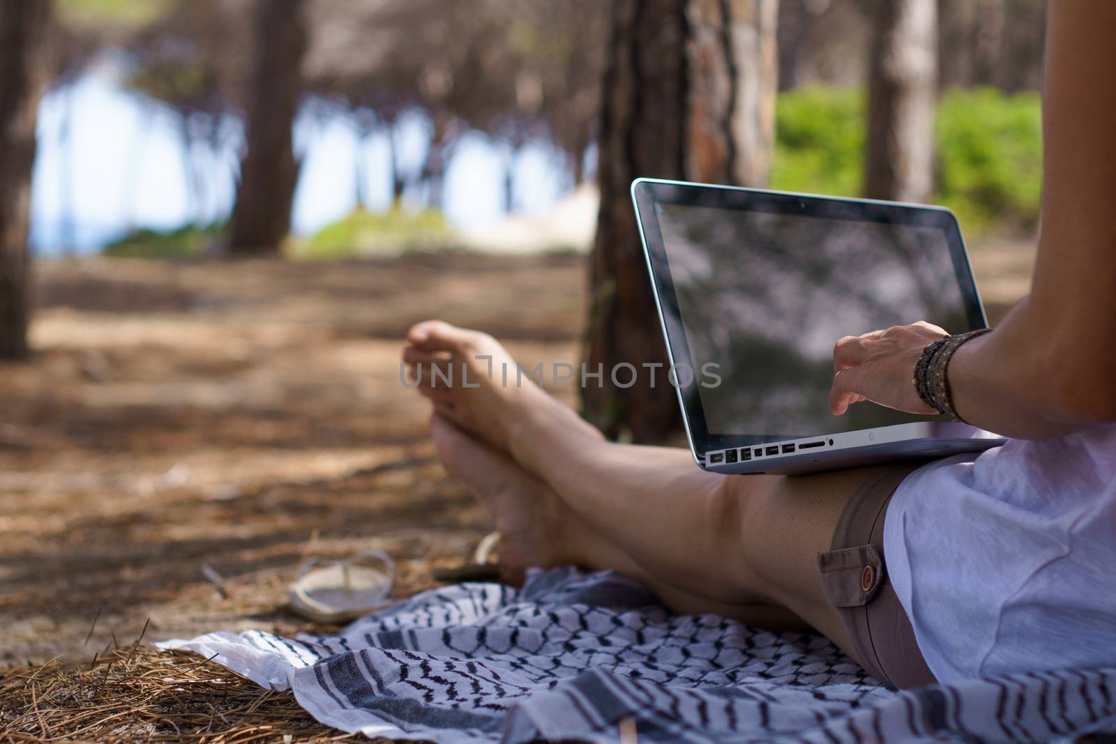 Close up of freelance woman working in vacation on the laptop sitting in a pine forest on the sea, smart working lifestyle concept theme and life choice by robbyfontanesi