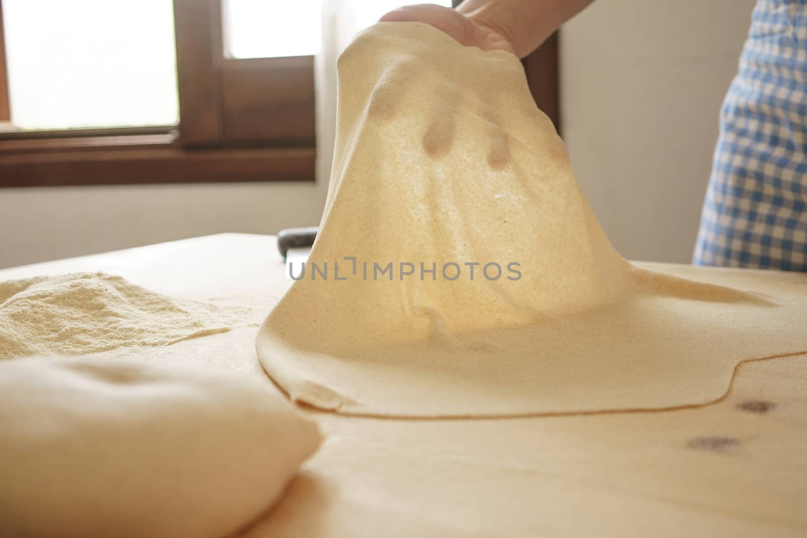 Making homemade fresh pasta: backlit woman hand show the transparency of the just rolled out fresh pasta, traditional Italian pasta, the woman cooks the food in the kitchen