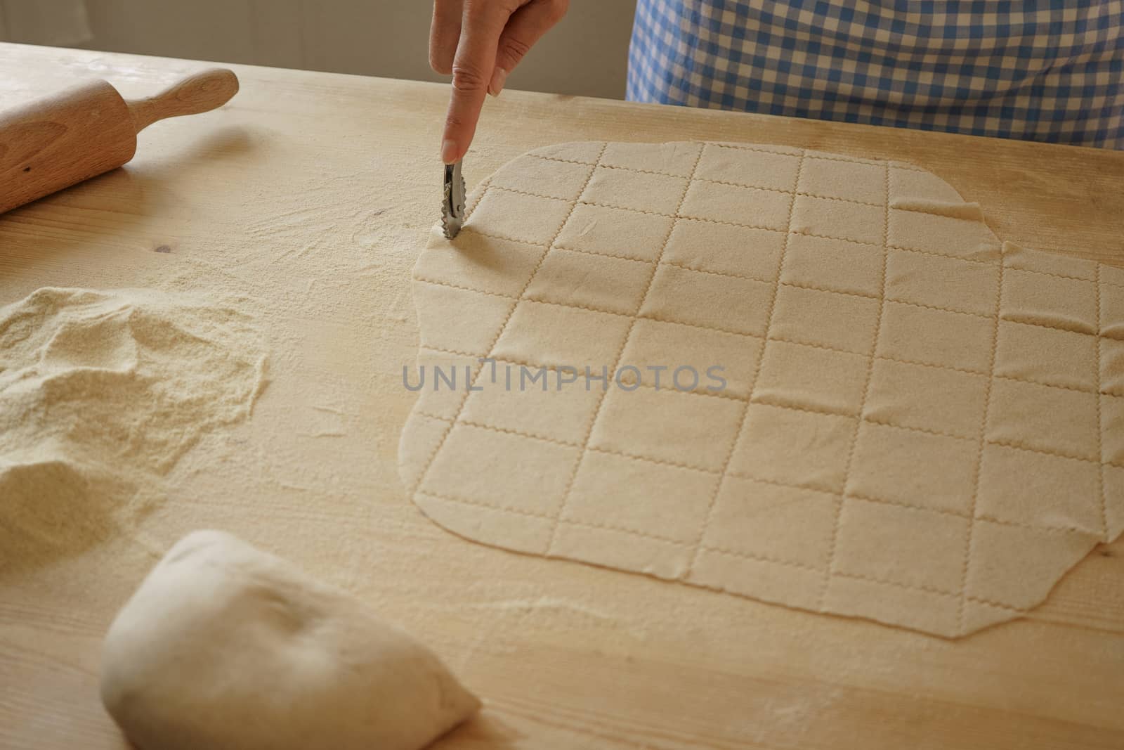 Close up process of homemade vegan farfalle pasta with durum wheat flour. The cook uses the rolling cutter to cut the dough, traditional Italian pasta, the woman cooks the food in the kitchen by robbyfontanesi