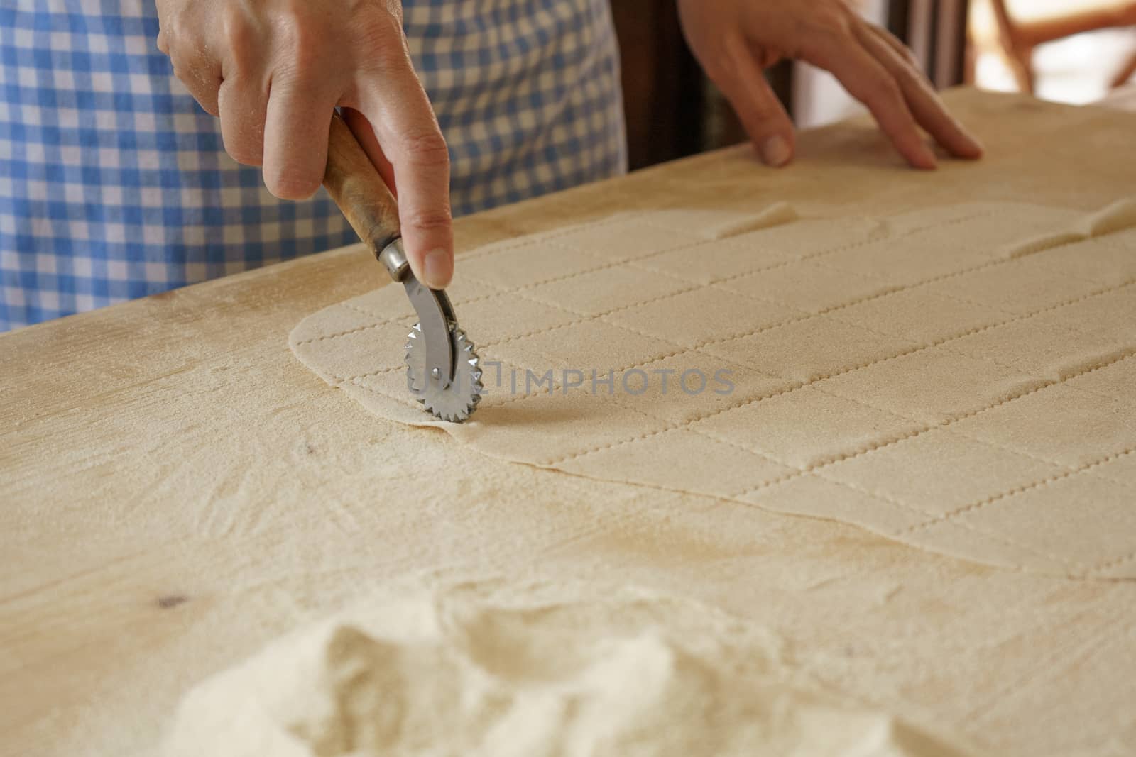 Close up process of homemade vegan farfalle pasta with durum wheat flour. The cook uses the rolling cutter to cut the dough, traditional Italian pasta, the woman cooks the food in the kitchen