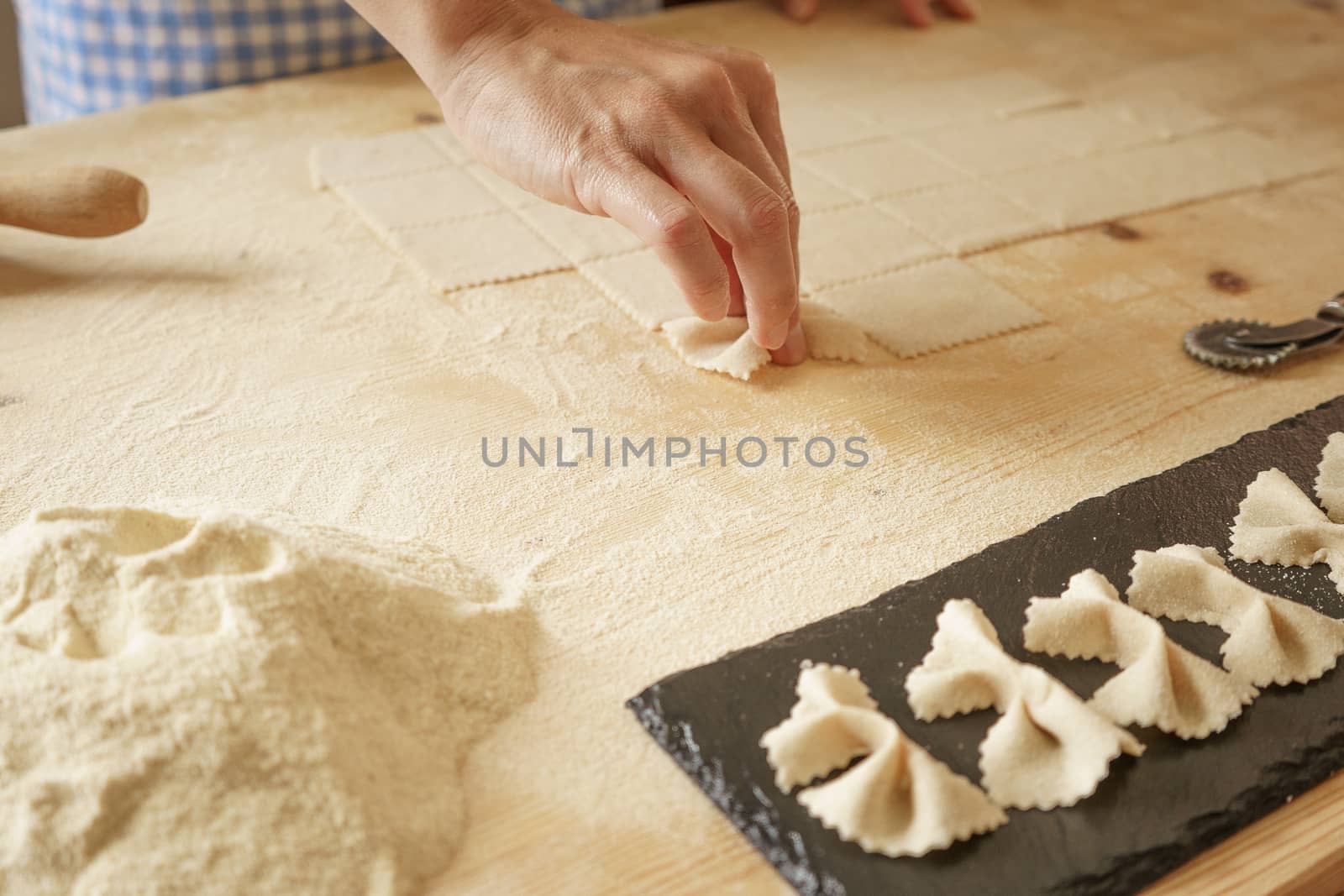 Close up process of homemade vegan farfalle pasta with durum wheat flour. The cook shapes the dough on the wooden cutting board, traditional Italian pasta, the woman cooks the food in the kitchen