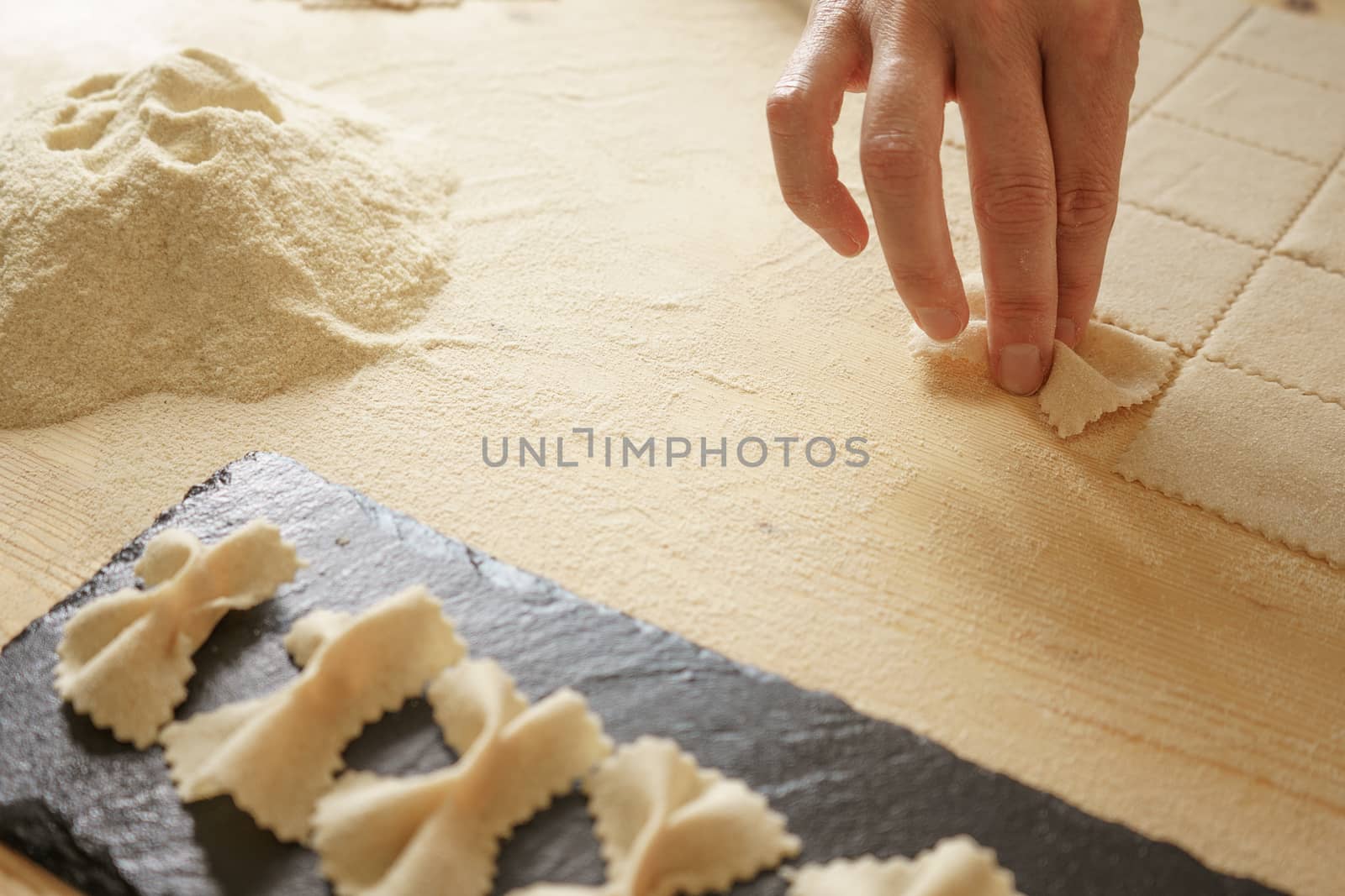 Close up detail of process of homemade vegan farfalle pasta with durum wheat flour. The cook kneads the dough on the wooden cutting board, traditional Italian pasta, the woman cooks the food by robbyfontanesi