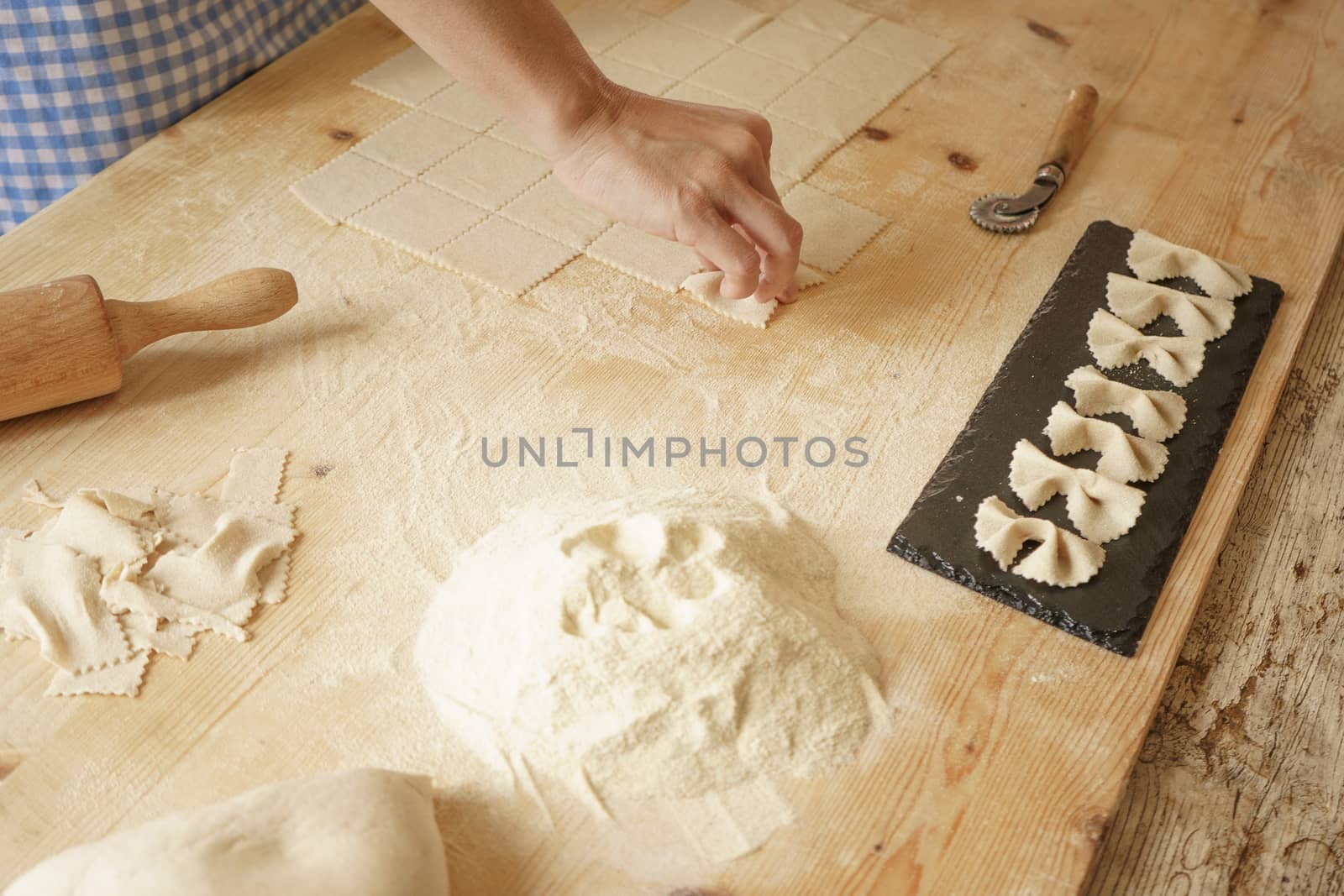 Close up process of homemade vegan farfalle pasta with durum wheat flour. The cook shapes the dough on the wooden cutting board, traditional Italian pasta, the woman cooks the food in the kitchen by robbyfontanesi