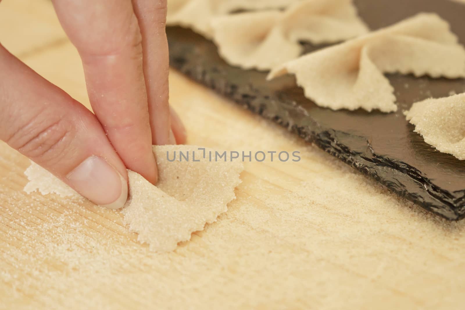 Close up detail of process of homemade vegan farfalle pasta with durum wheat flour. The cook kneads the dough on the wooden cutting board, traditional Italian pasta, the woman cooks the food