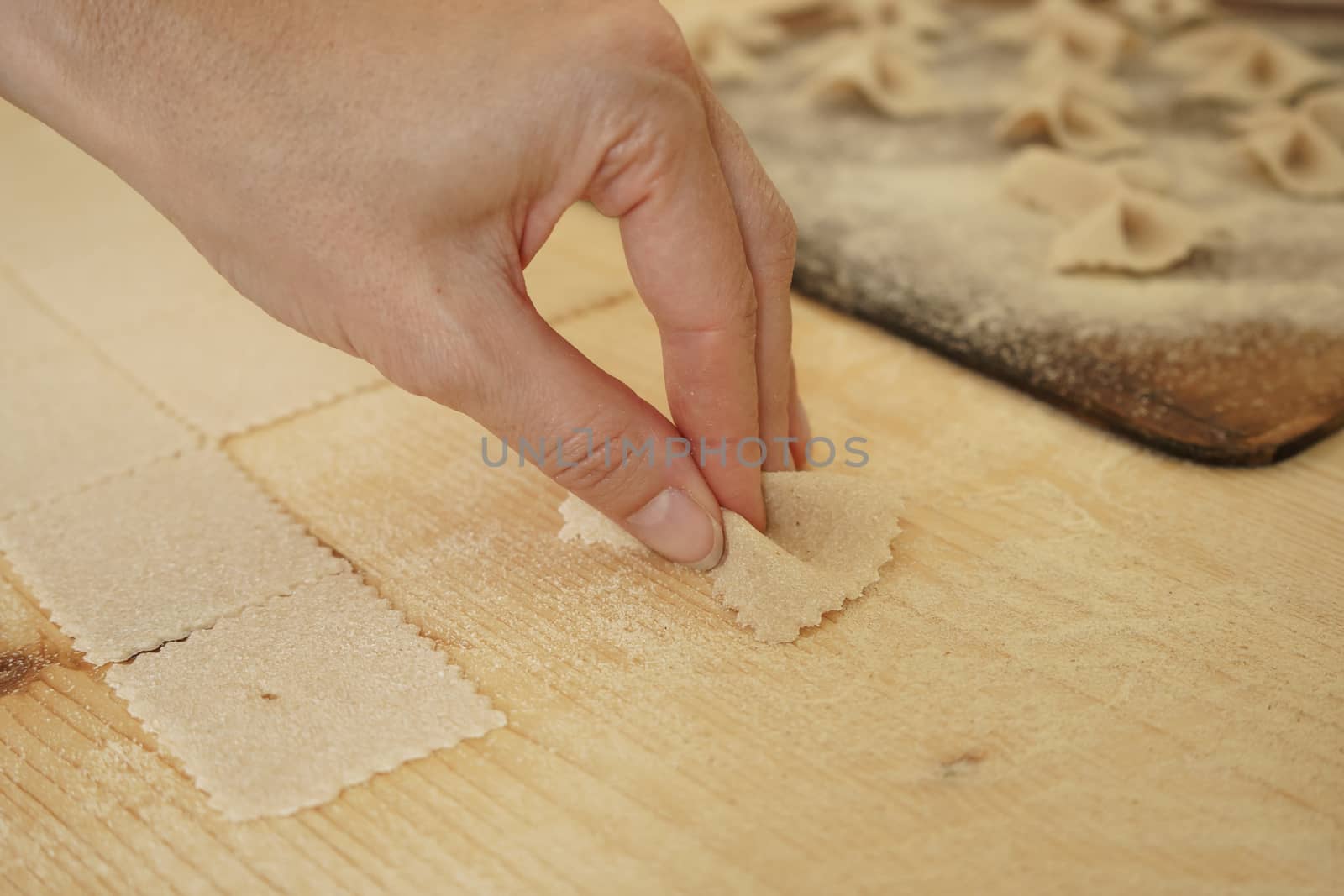 Close up macro detail of process of homemade vegan farfalle pasta with durum wheat flour. The cook kneads the dough on the wooden cutting board, traditional Italian pasta, the woman cooks the food