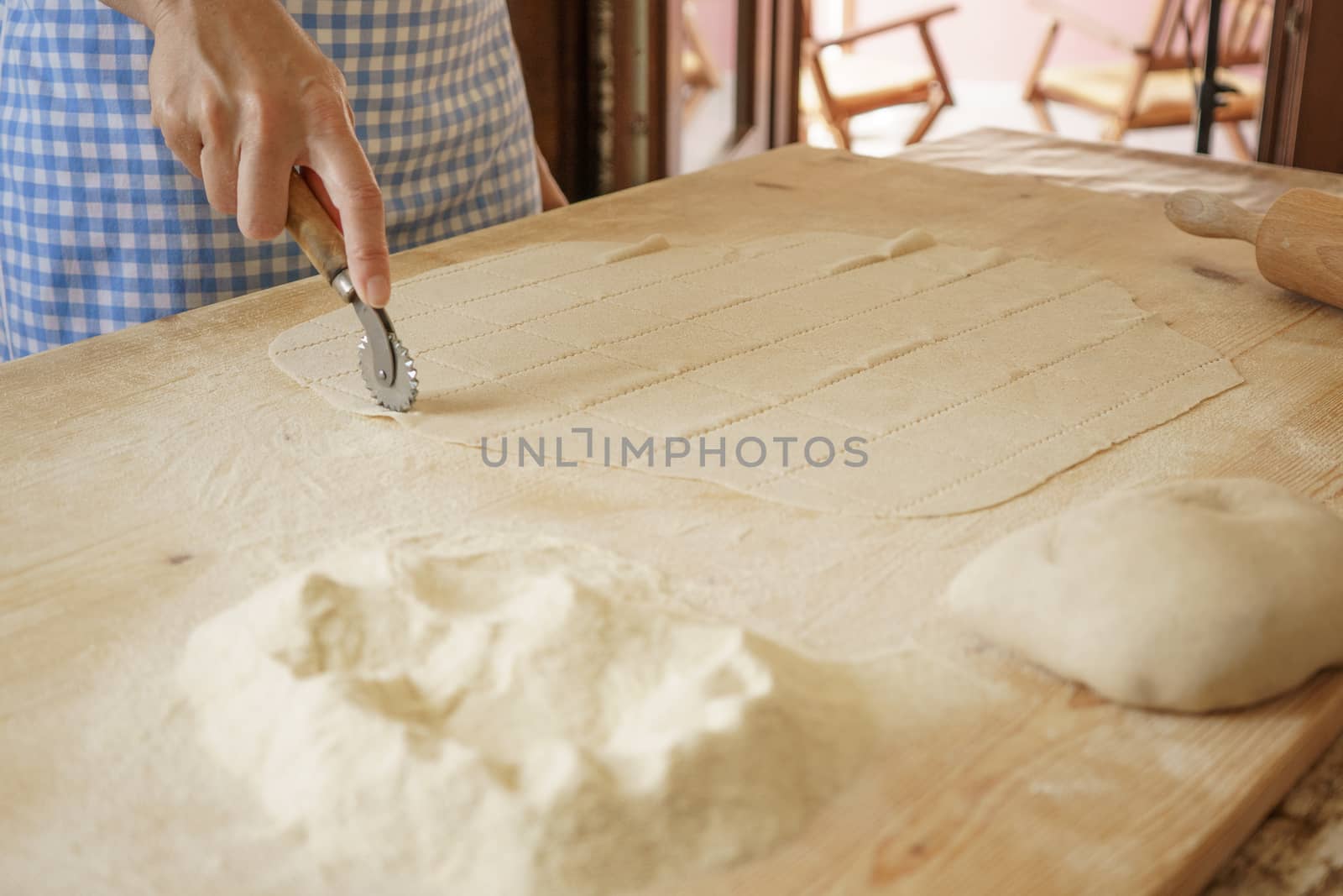 Close up process of homemade vegan farfalle pasta with durum wheat flour. The cook uses the rolling cutter to cut the dough, traditional Italian pasta, the woman cooks the food in the kitchen by robbyfontanesi