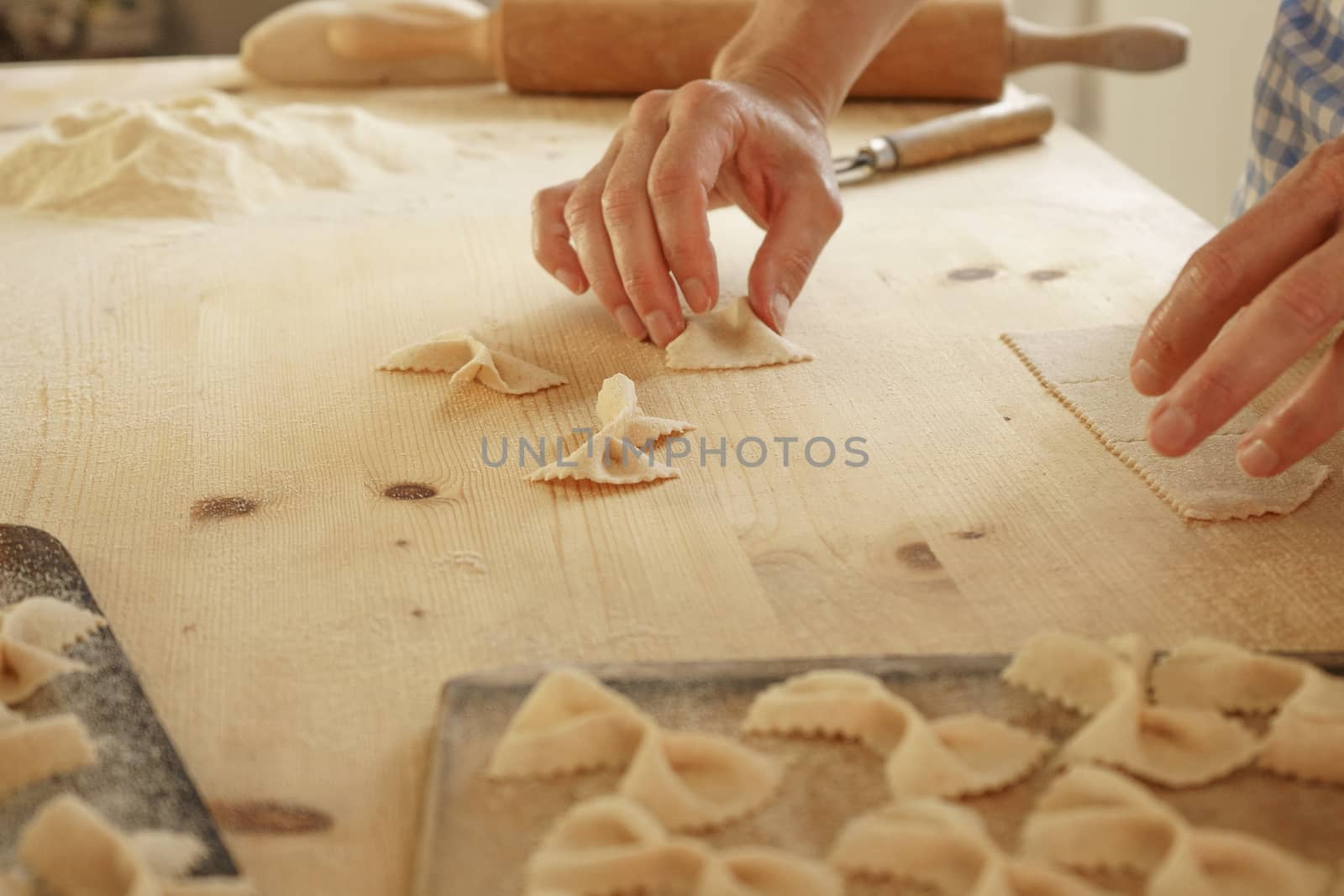 Close up process of homemade vegan farfalle pasta with durum wheat flour. The cook shapes the dough on the wooden cutting board, traditional Italian pasta, the woman cooks the food in the kitchen by robbyfontanesi
