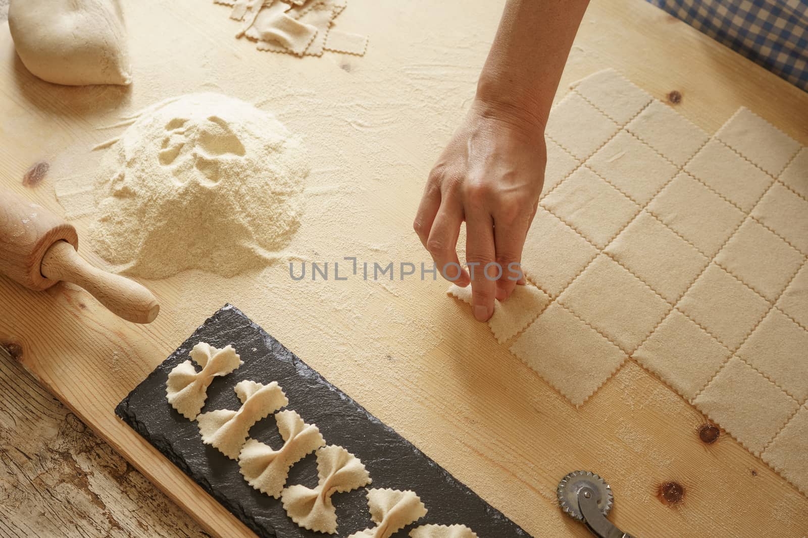 Close up process of homemade vegan farfalle pasta with durum wheat flour. The cook shapes the dough on the wooden cutting board, traditional Italian pasta, the woman cooks the food in the kitchen