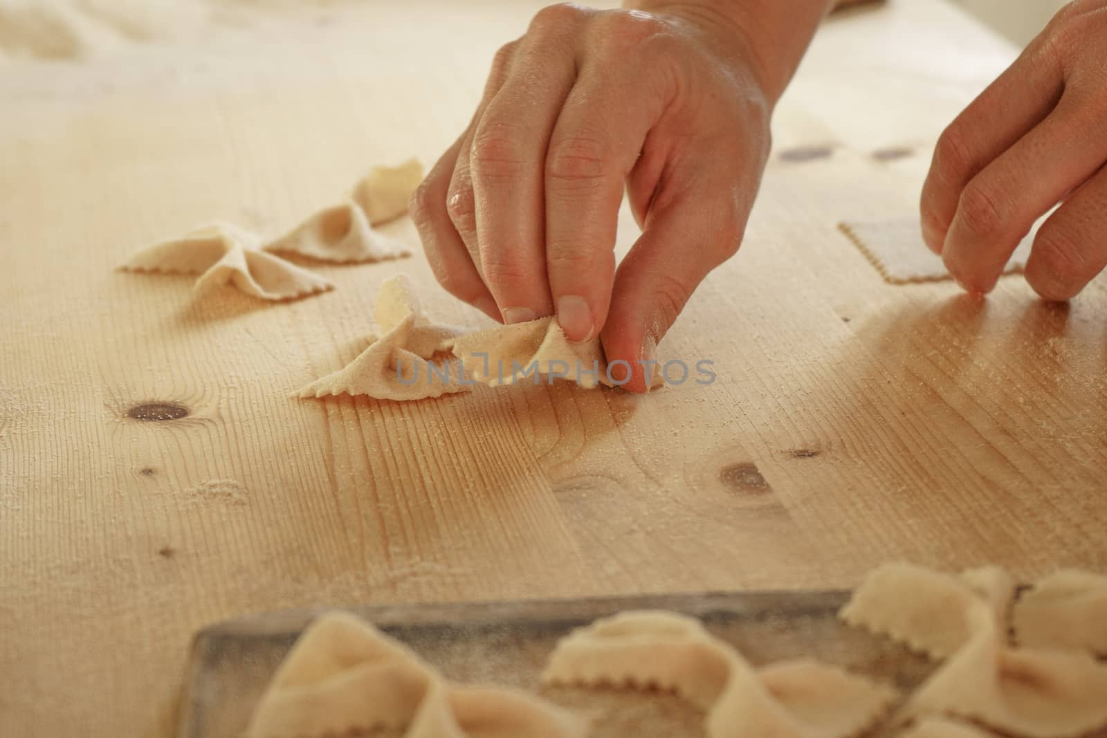 Close up process of homemade vegan farfalle pasta with durum wheat flour. The cook shapes the dough on the wooden cutting board, traditional Italian pasta, the woman cooks the food in the kitchen by robbyfontanesi