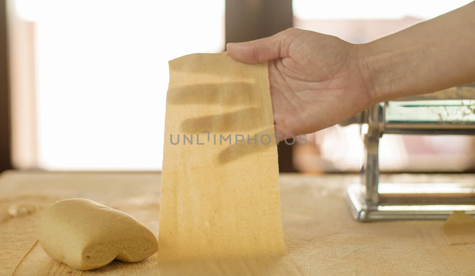 Making homemade fresh pasta: backlit woman hand show the transparency of the just rolled out fresh pasta