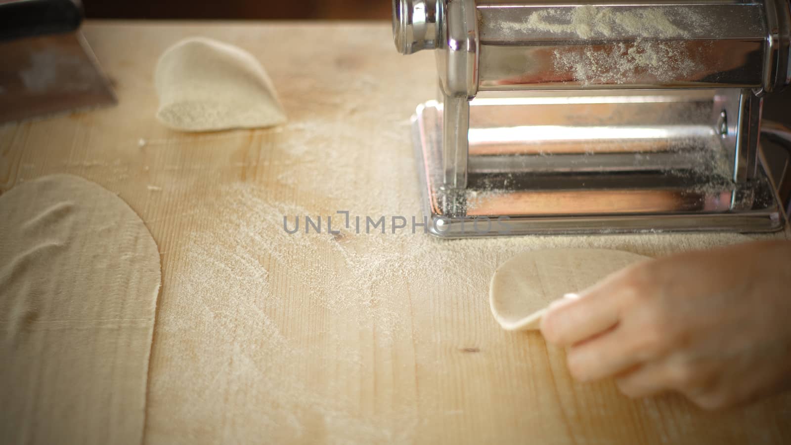 Making fresh homemade pasta: overhead top view of woman's hand pulling out the rolled dough from the manual pasta making machine backlit by robbyfontanesi