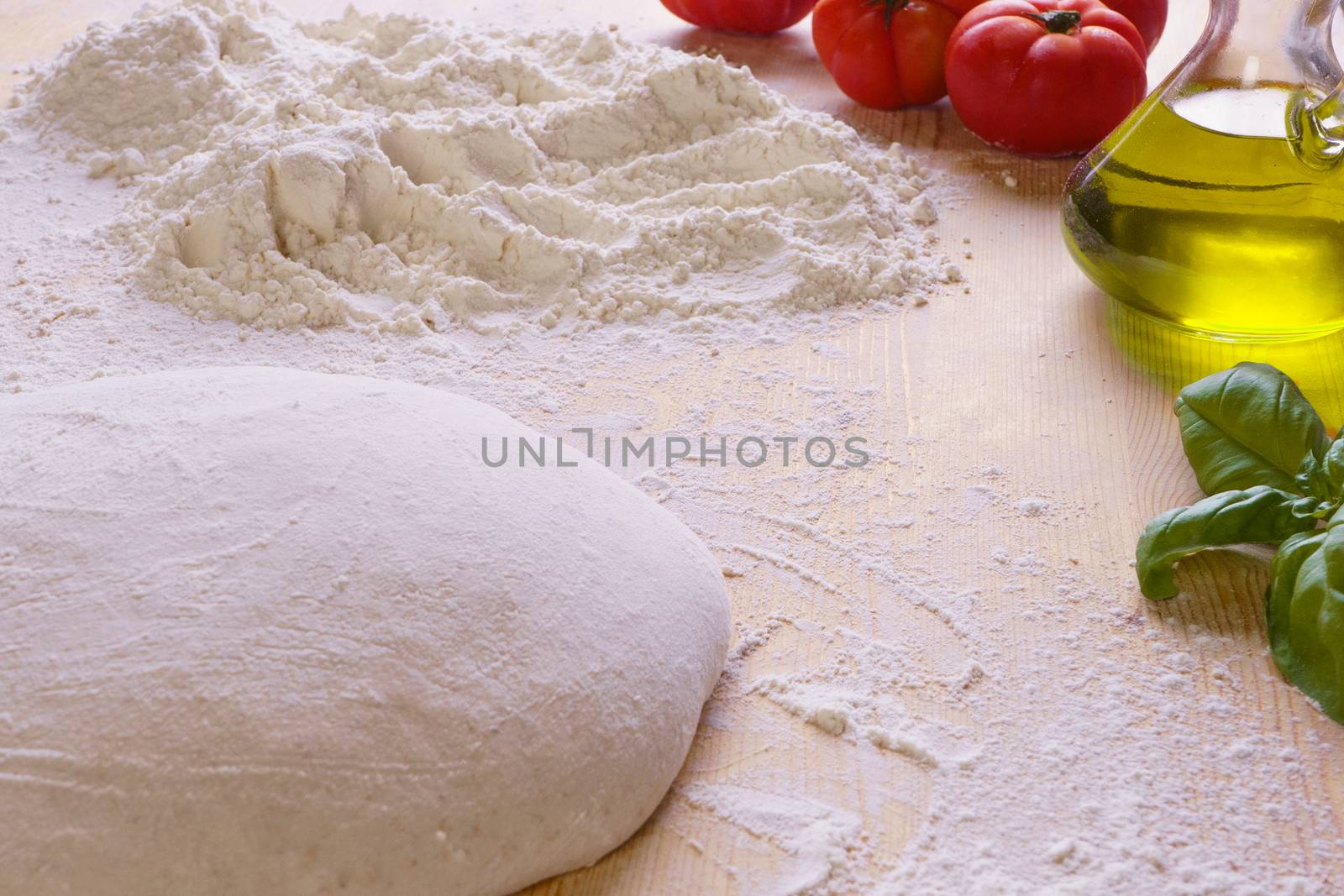 Macro close up of bread or pizza dough on wooden worktop and flour, extra virgin oil, tomatoes and basil in the background