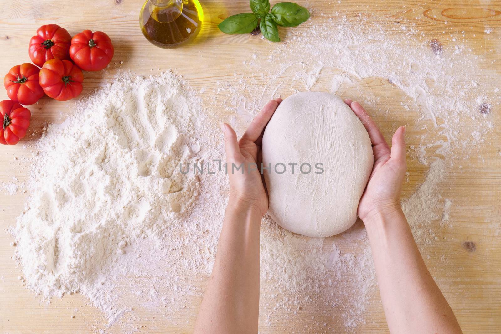 Flat lay top view of woman chef hands kneading pizza dough on wooden worktop and flour, extra virgin oil, tomatoes and basil