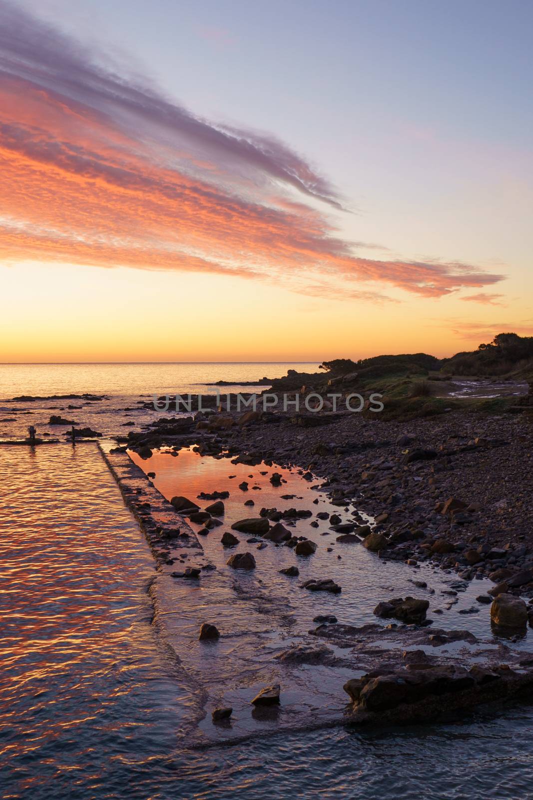 Orange and red sky with gorgeous cloud on an old abandoned sea pier in dawn or sunset with water reflections between the rocks