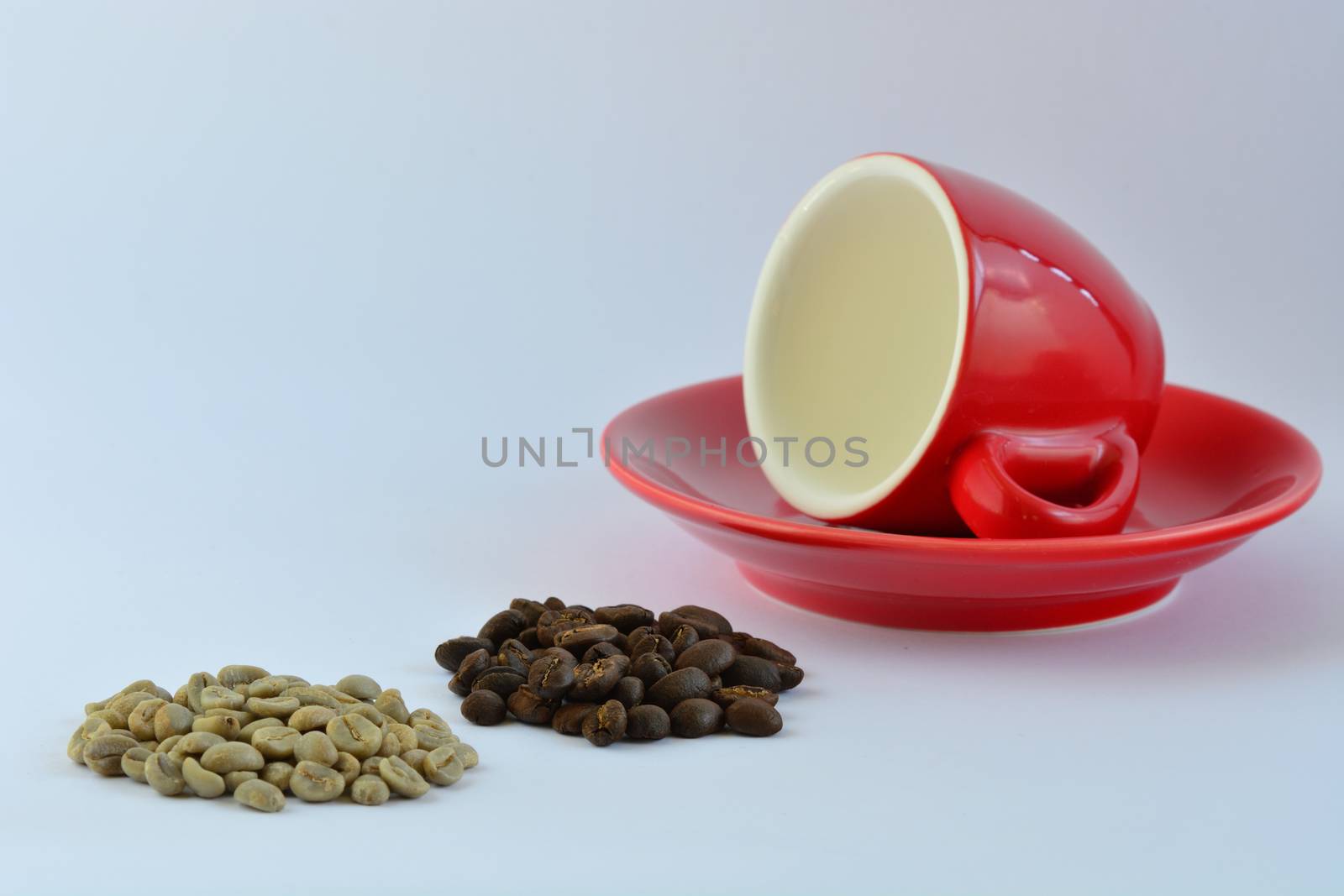 A close-up photo of a bright red espresso coffee cup, some green coffee beans and some roasted coffee beans on white background.