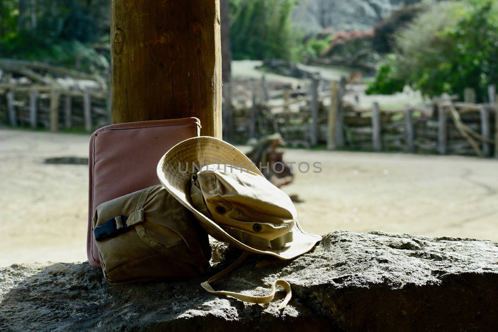 A close-up photo of an old weathered cowboy hat and a travel bag, left on stone in the wilderness. by Marshalkina