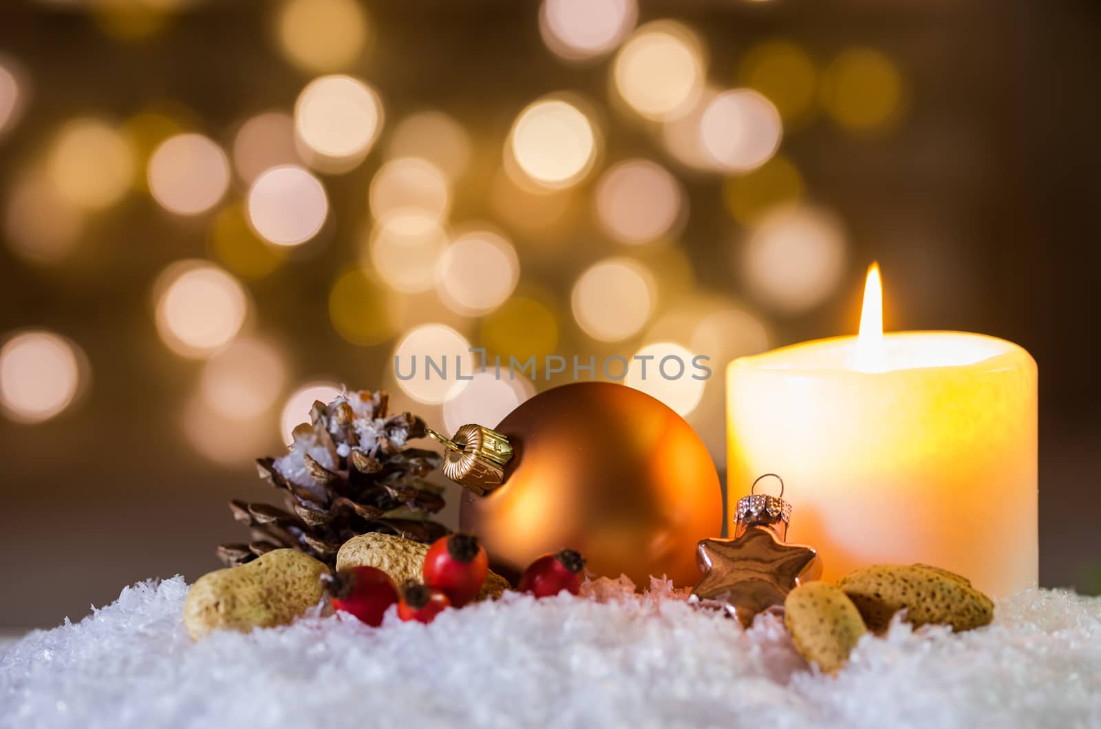 Burning candle and Christmas decoration over snow and blurred lights background with festive mood