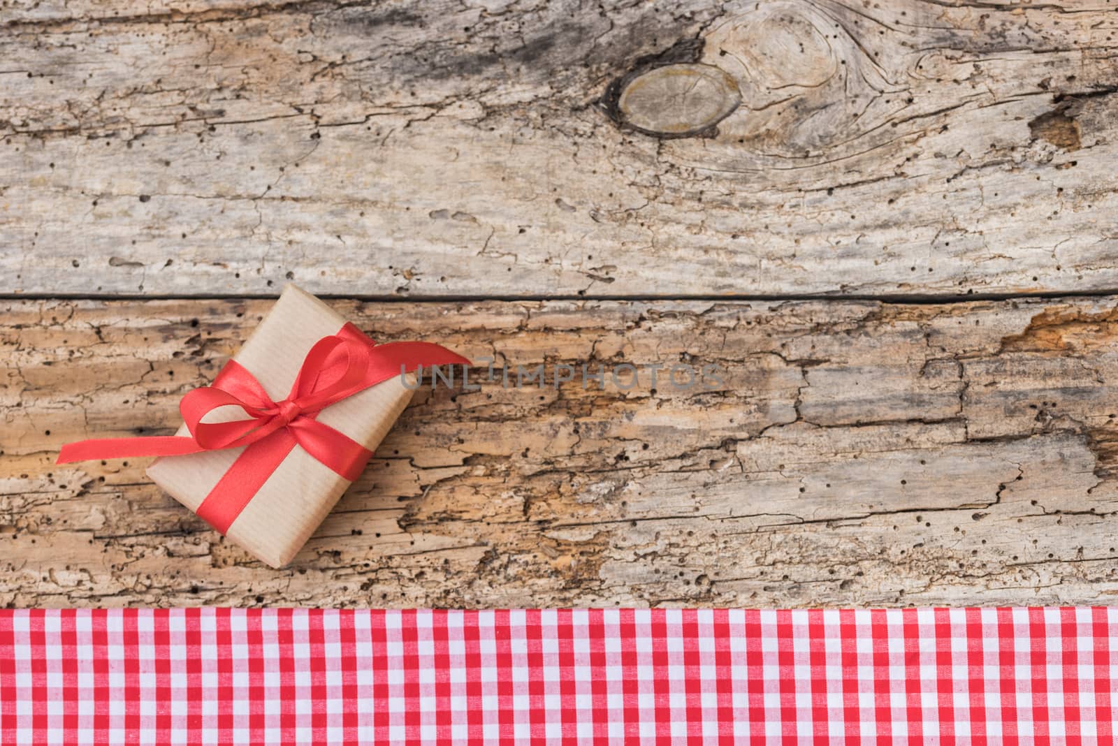 Christmas gift on rustic wood table and red checkered border, copy space