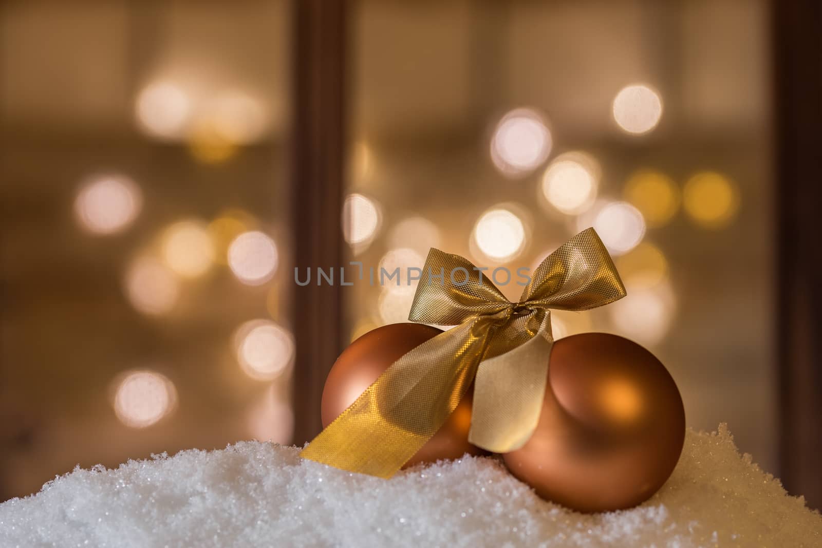 Two golden Christmas balls with ribbon on snow with blurred lights background