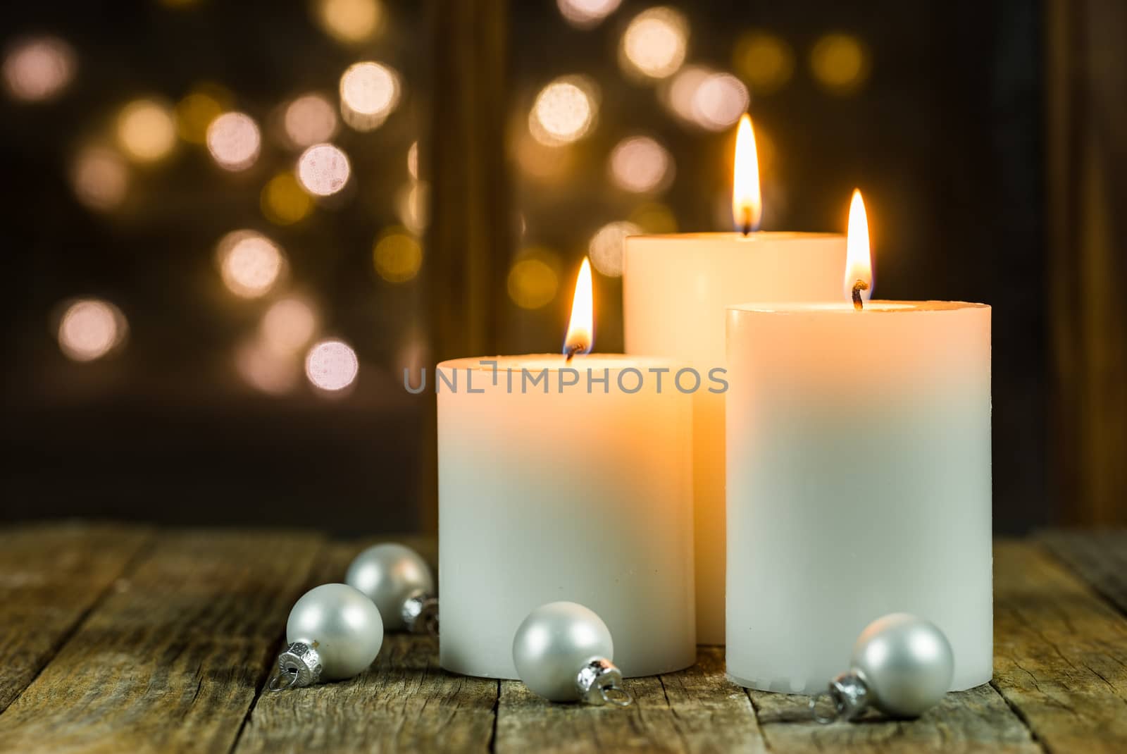Christmas or Advent candles on wooden table in front of window lights background