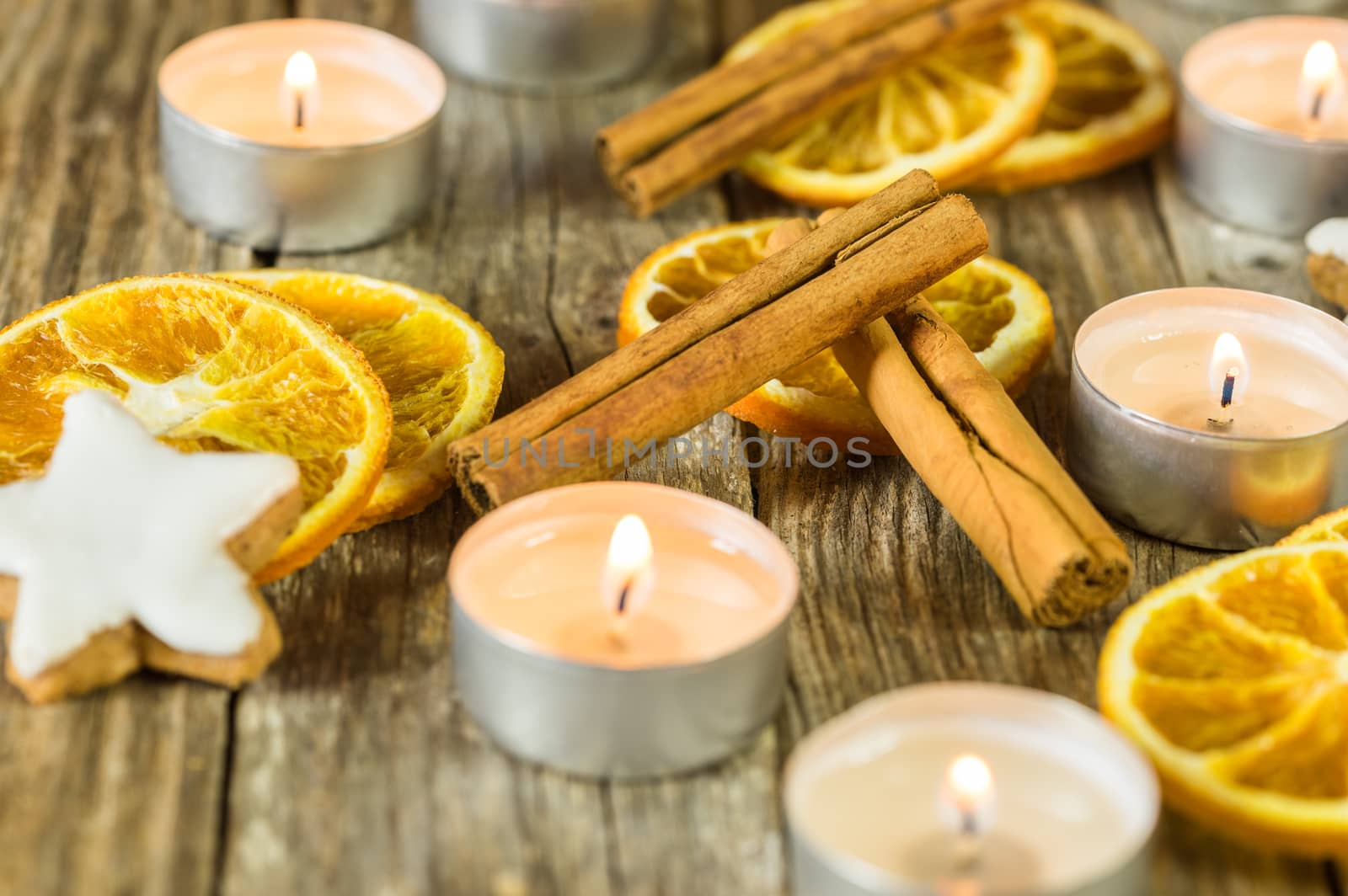Christmas season decoration with candle flames, star shape cookies, cinnamon spice and orange slices