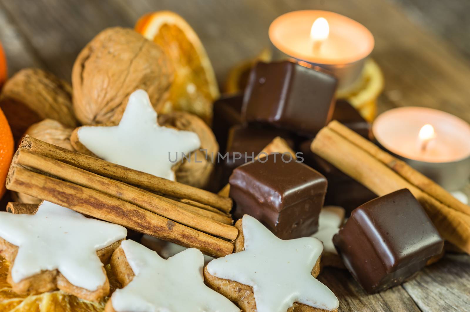 Christmas star shape cookies, chocolate, nuts, cinnamon and candles on wooden table