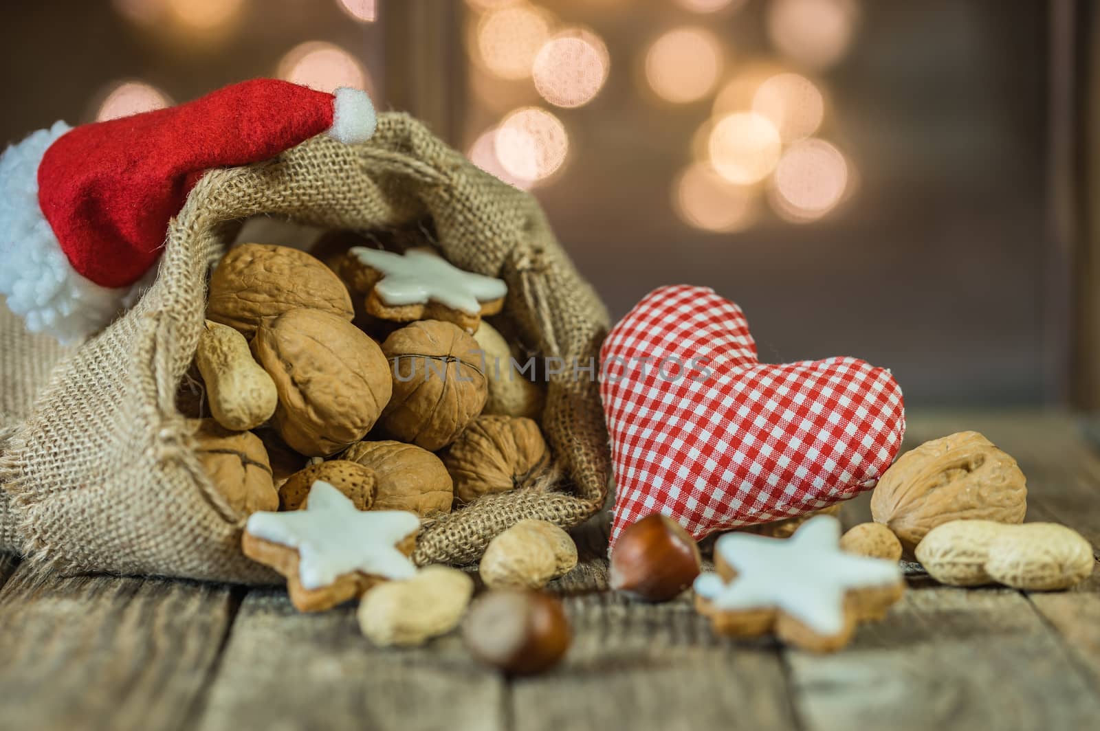 Christmas heart with nuts and star shape cookies in Santa Claus bag with red cap on wooden table