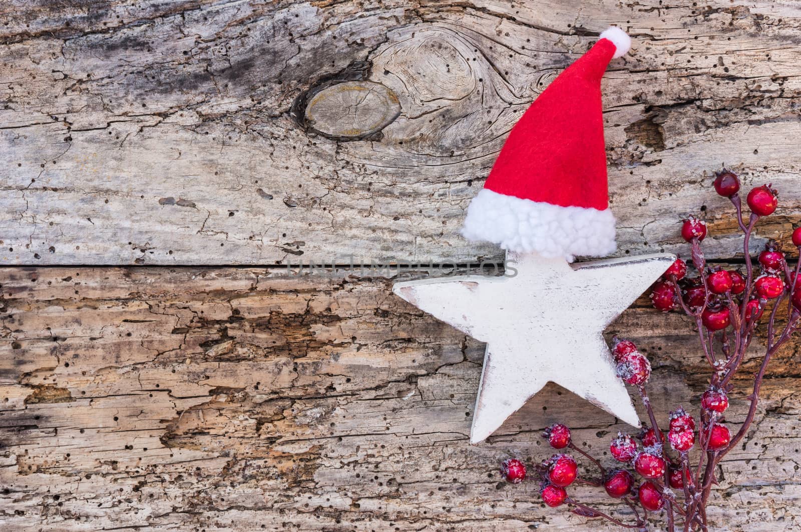 Christmas or Advent decoration with wooden star shape, santa claus cap an red berries on wood