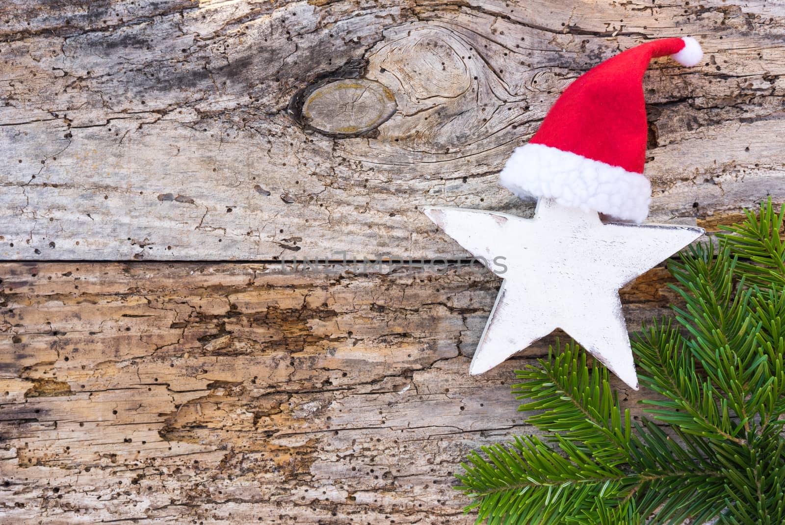 Advent and Christmas decoration with star shape, red Santa Claus hat and green fir tree branch on wood, top view