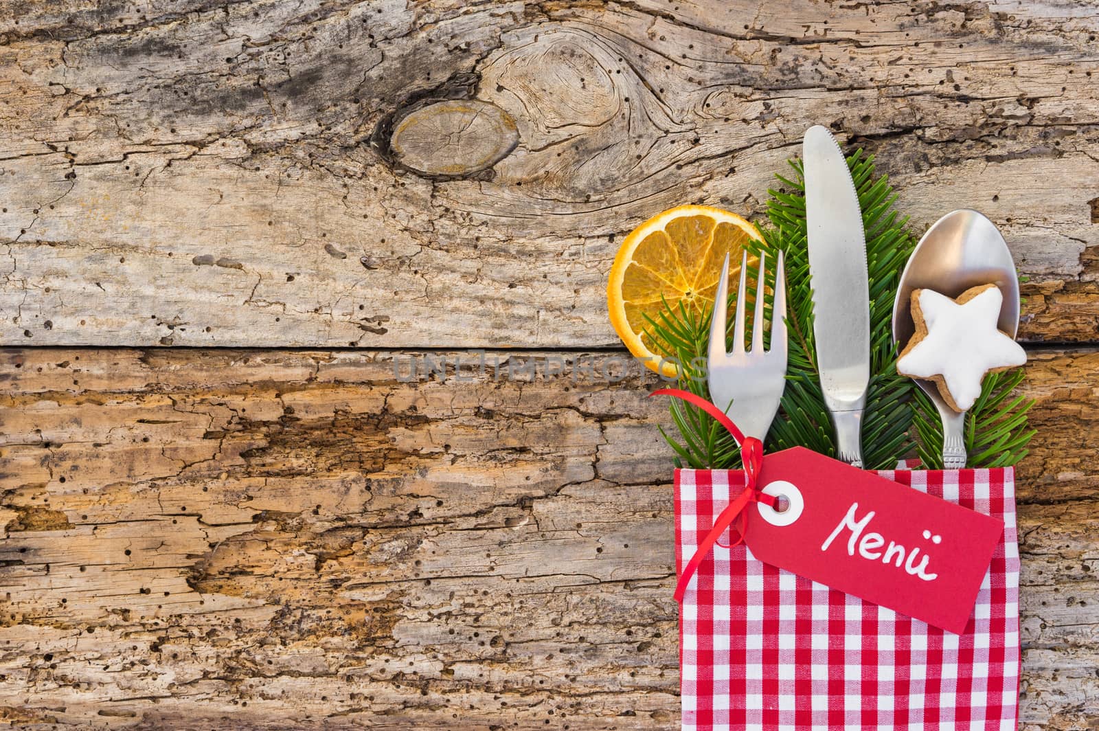 Christmas cutlery with tag and german word menue, means menu, on rustic wooden table background