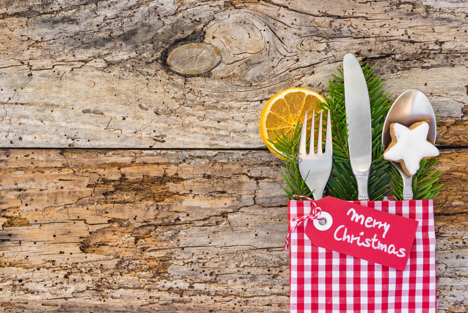 Christmas dinner cutlery with napkin on rustic wooden table, top view and tag Merry Christmas