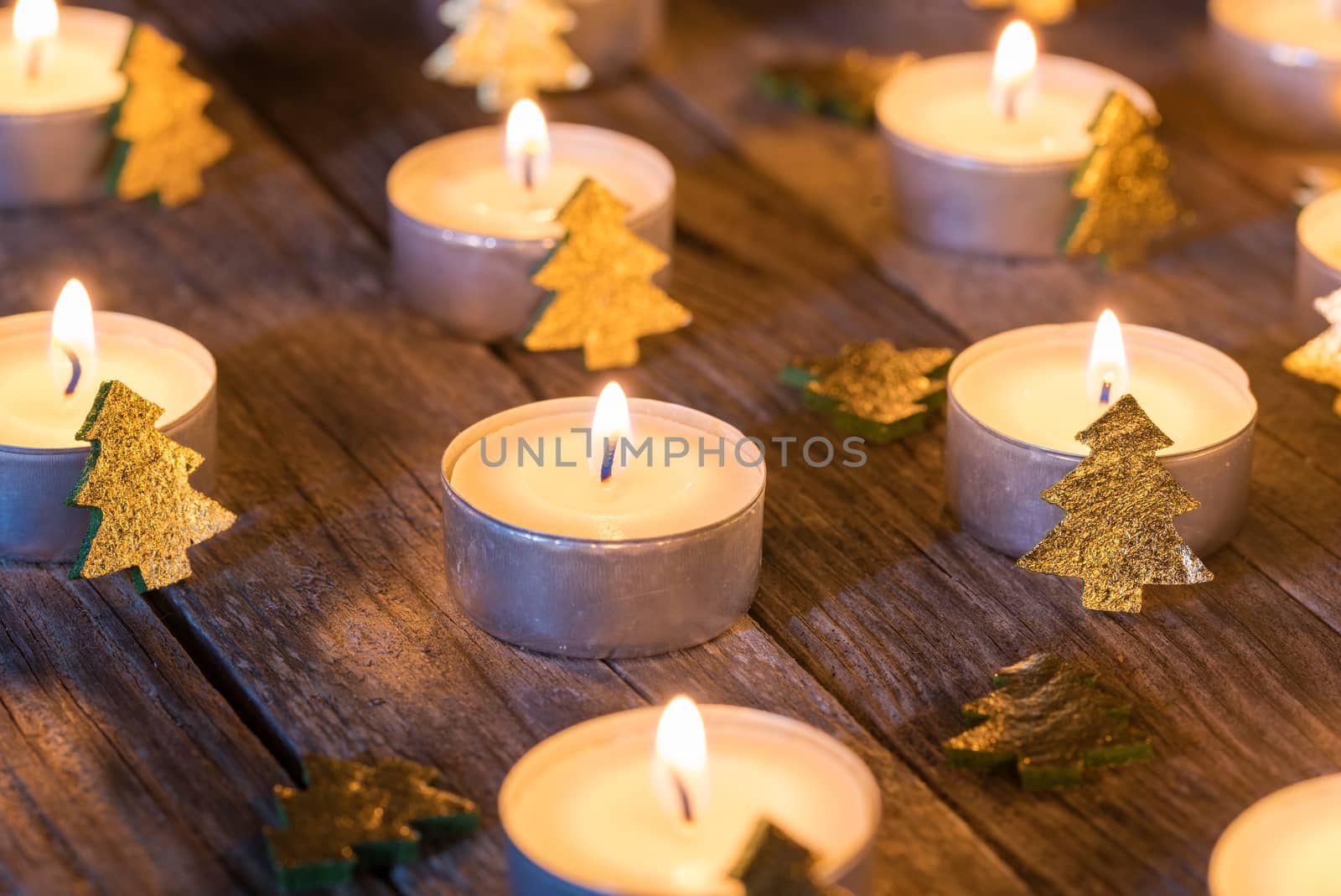 Close-up of white burning candle flames with golden christmas tree decoration on wooden table